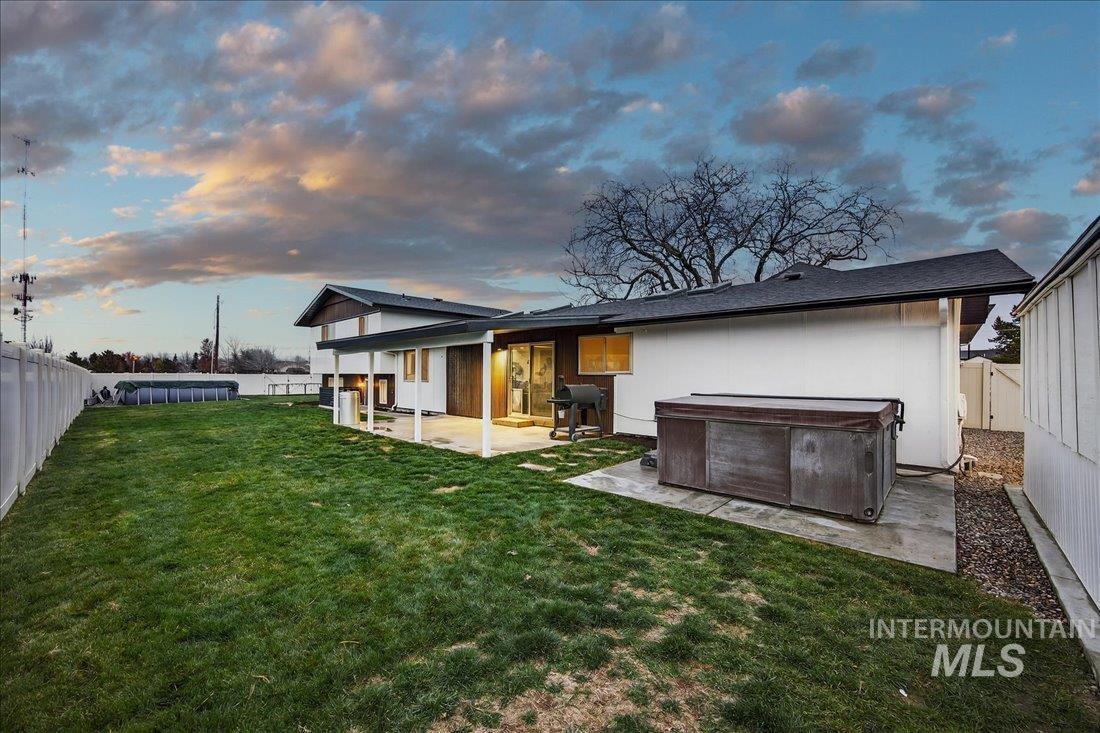 Back of house at dusk with a hot tub, a fenced backyard, a patio area, and a swimming pool