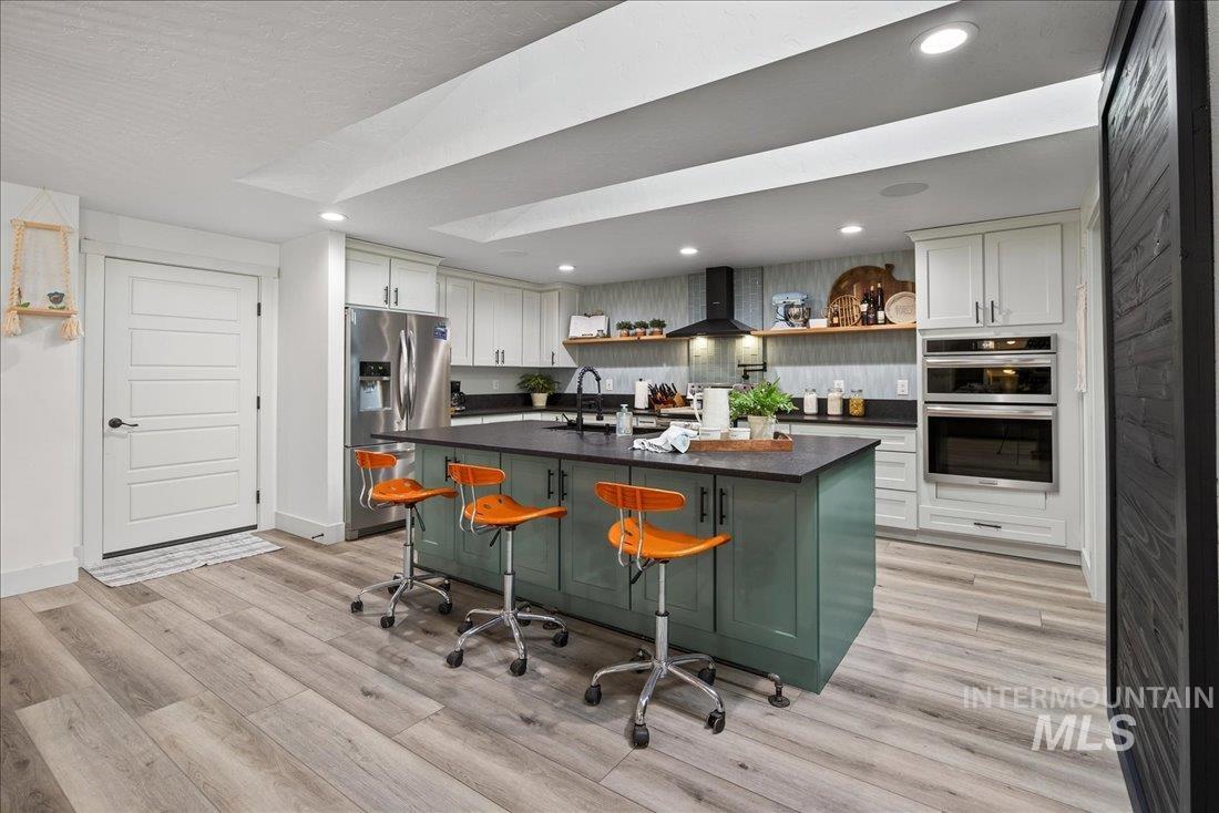 Kitchen with open shelves, green cabinetry, stainless steel appliances, recessed lighting, and a kitchen island with sink