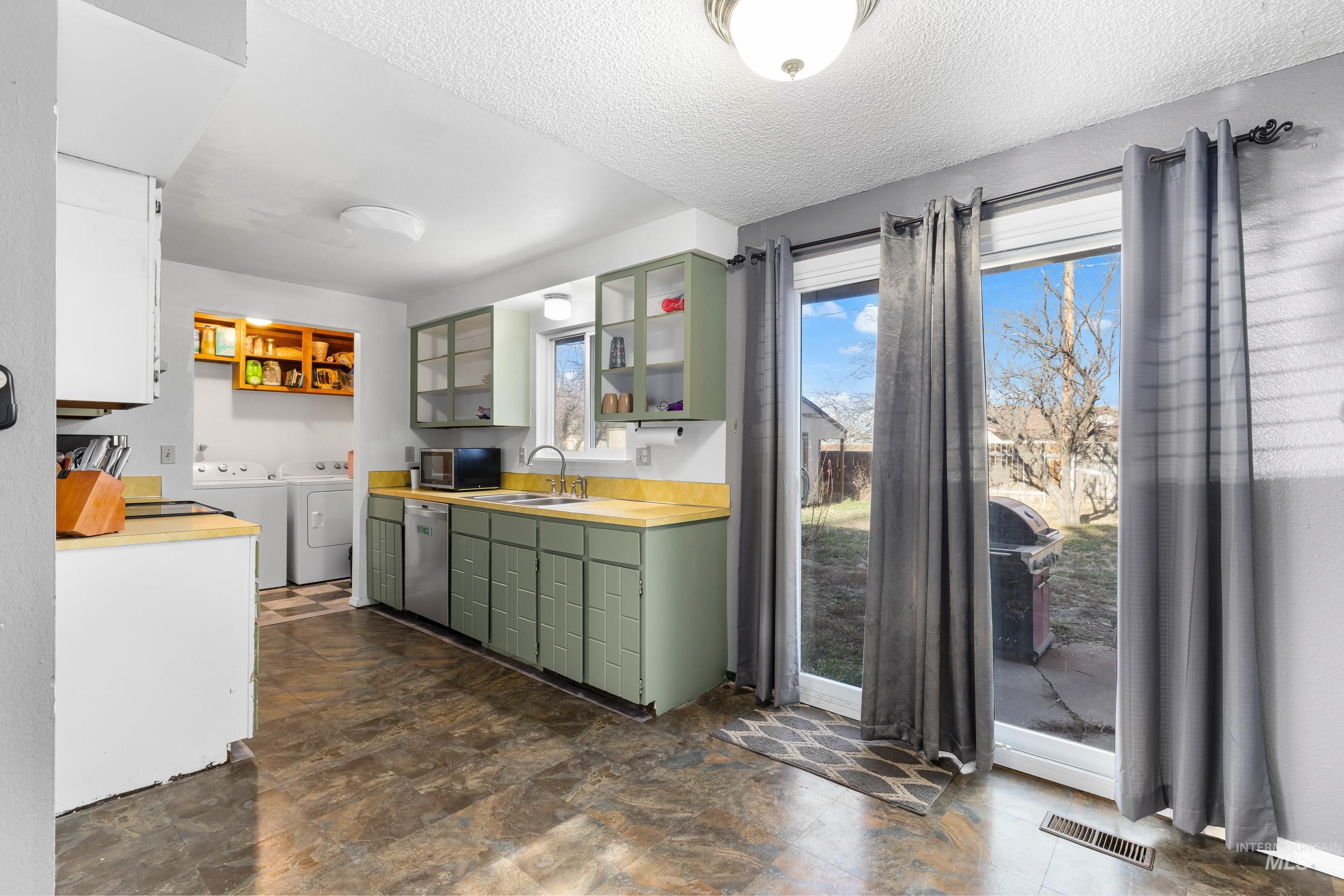 Kitchen featuring light countertops, washing machine and clothes dryer, a textured ceiling, stainless steel dishwasher, and glass insert cabinets