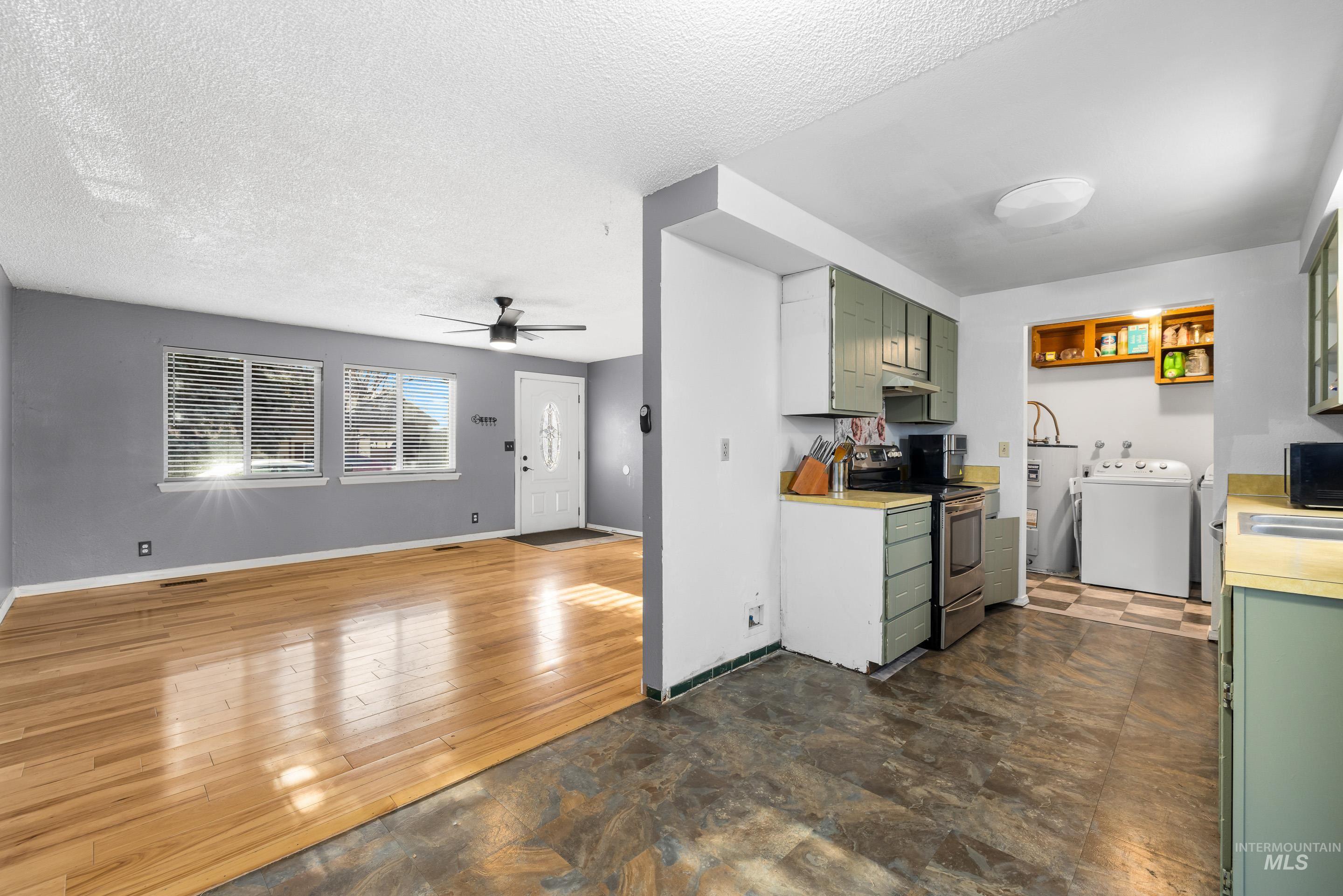 Kitchen featuring green cabinets, light countertops, open floor plan, stainless steel range with electric stovetop, and a textured ceiling