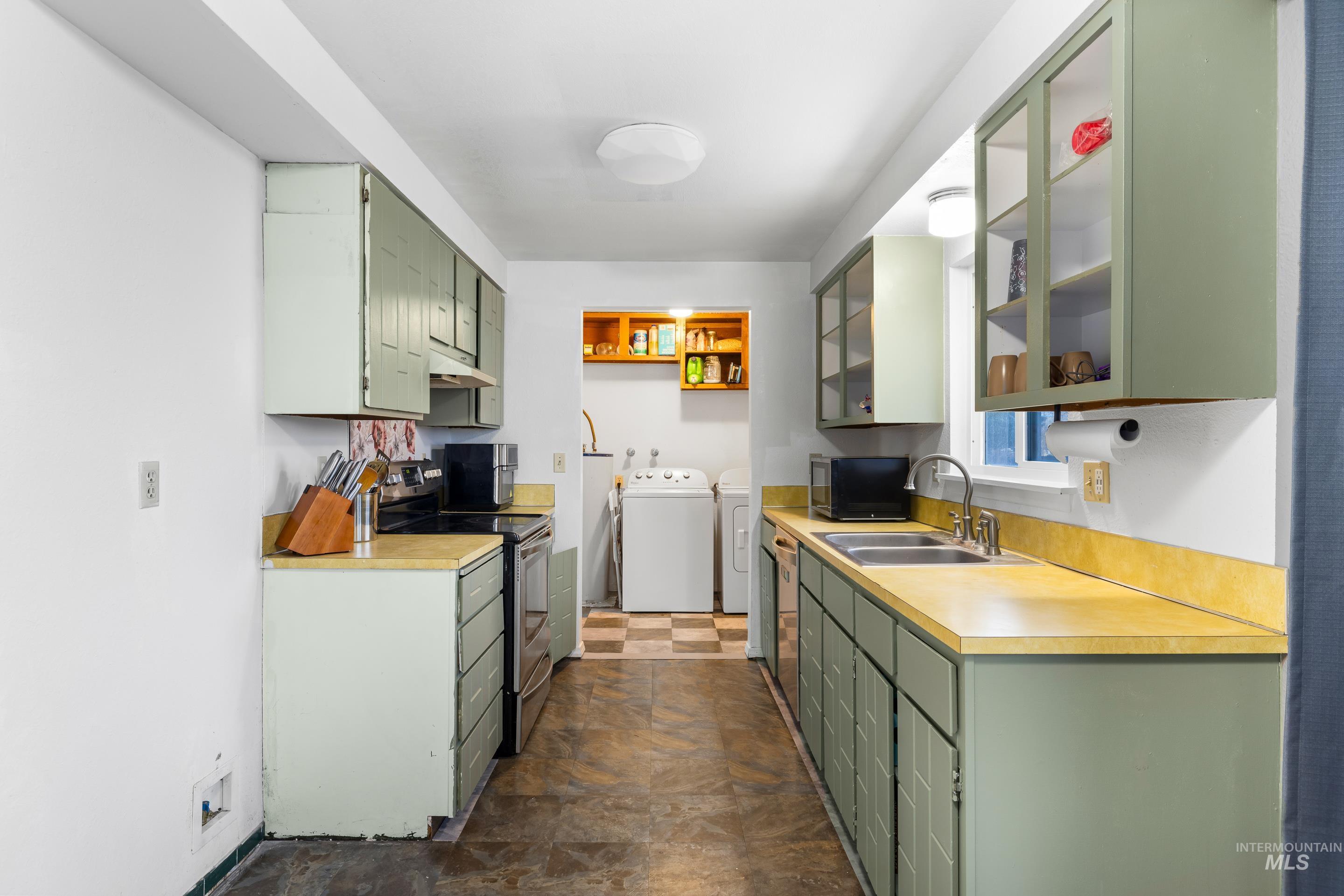Kitchen with green cabinets, stainless steel electric range oven, light countertops, glass insert cabinets, and independent washer and dryer