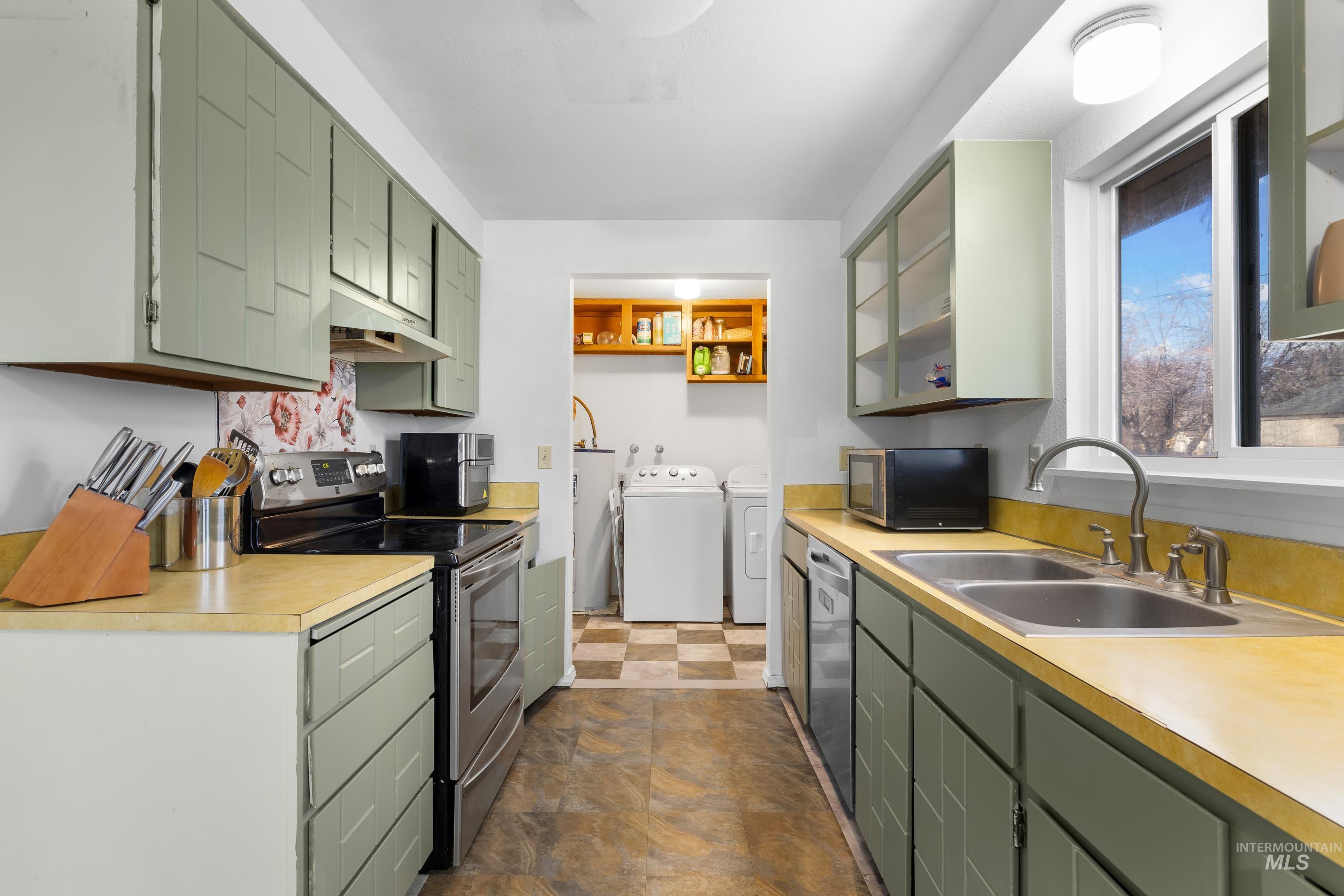 Kitchen with green cabinets, stainless steel appliances, washing machine and dryer, light countertops, and under cabinet range hood