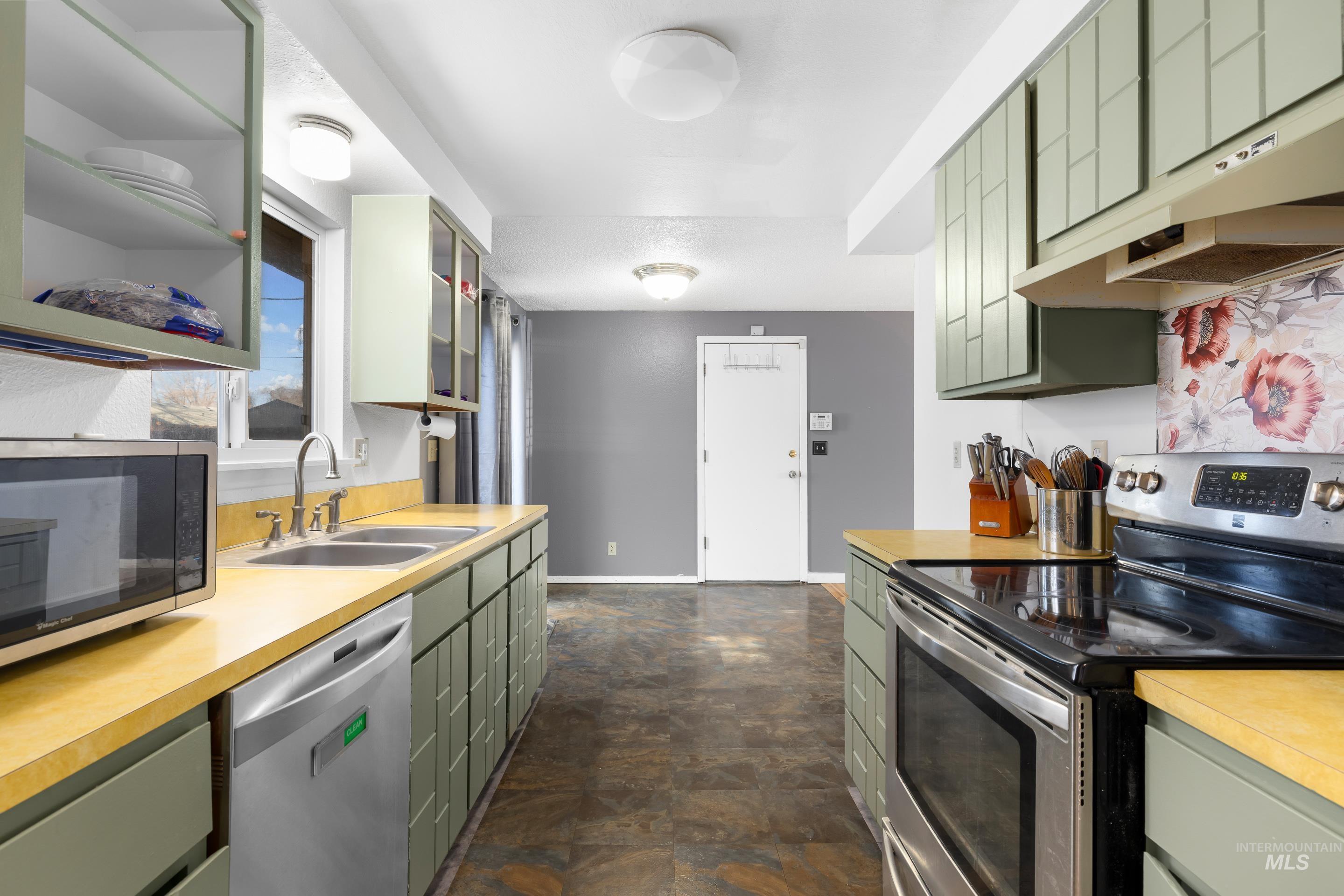 Kitchen with green cabinets, appliances with stainless steel finishes, light countertops, and under cabinet range hood