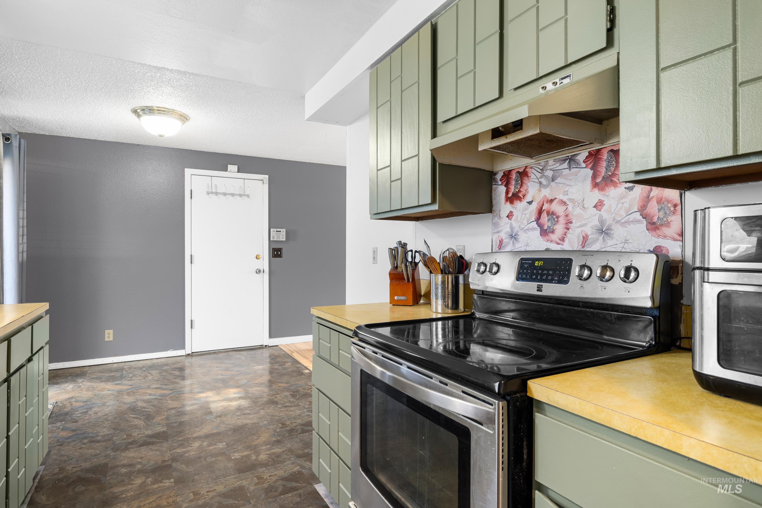 Kitchen featuring green cabinetry, stainless steel electric range, under cabinet range hood, light countertops, and a textured ceiling