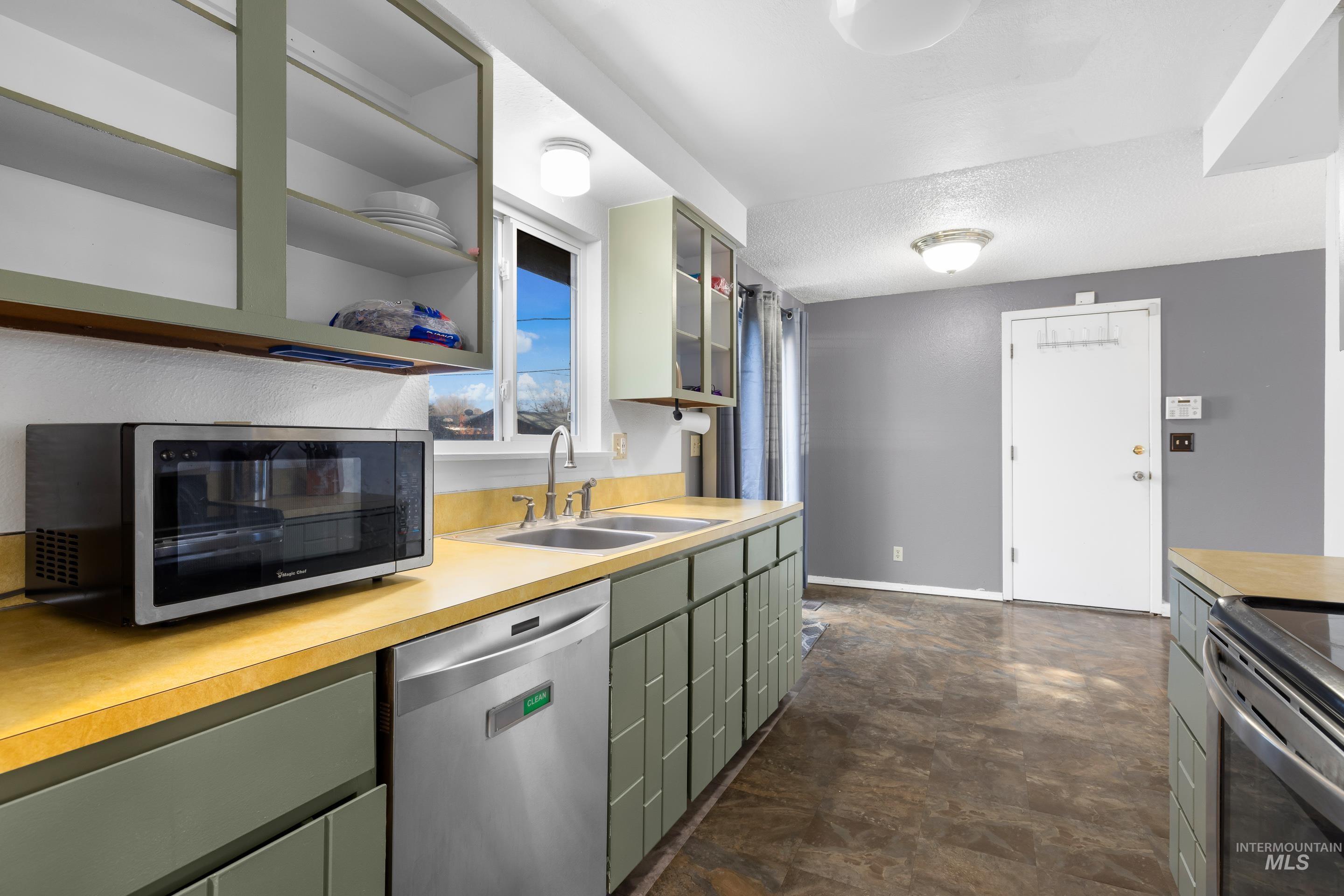 Kitchen featuring appliances with stainless steel finishes, light countertops, stone finish floors, green cabinetry, and glass insert cabinets