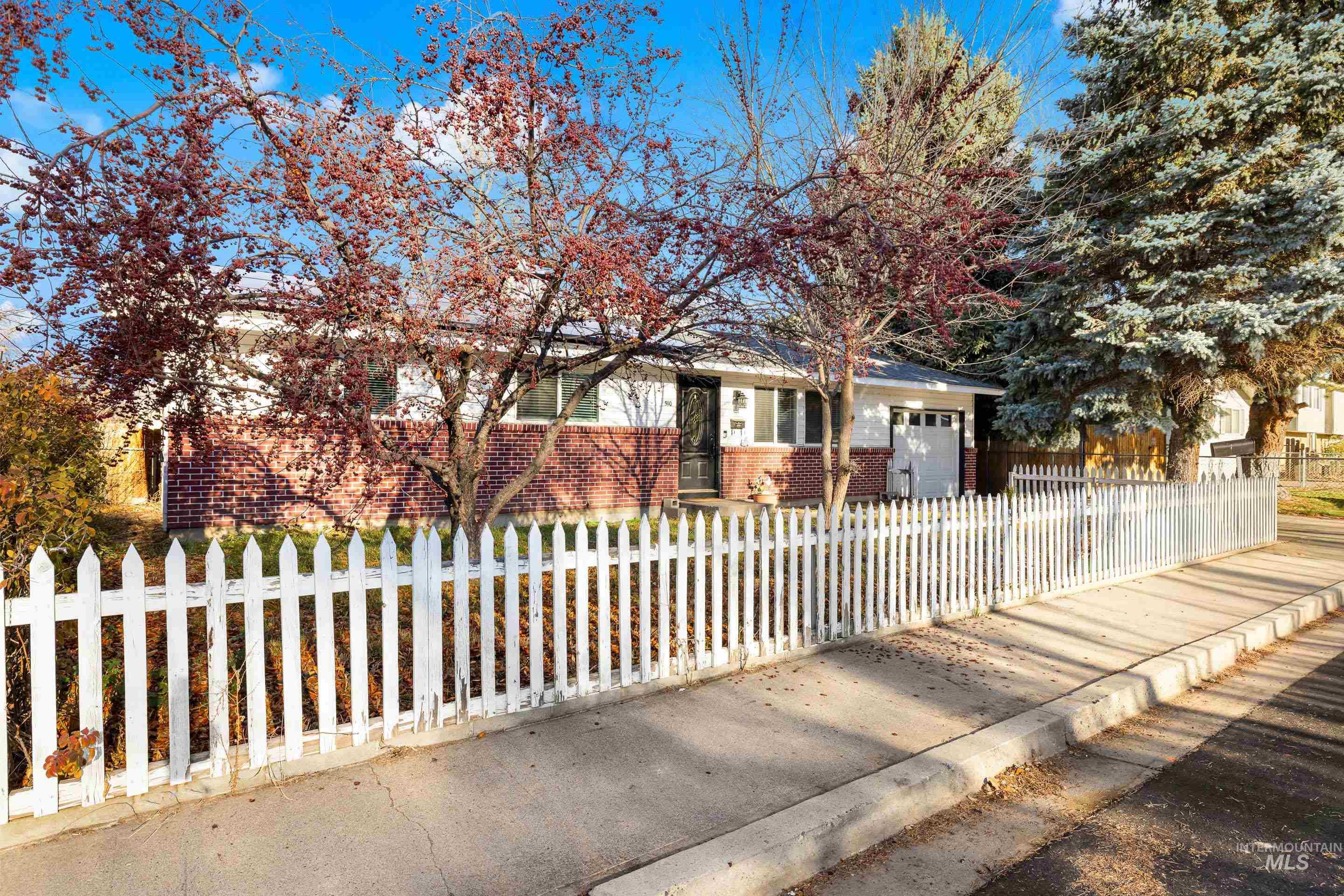 View of property hidden behind natural elements with brick siding, a fenced front yard, and an attached garage
