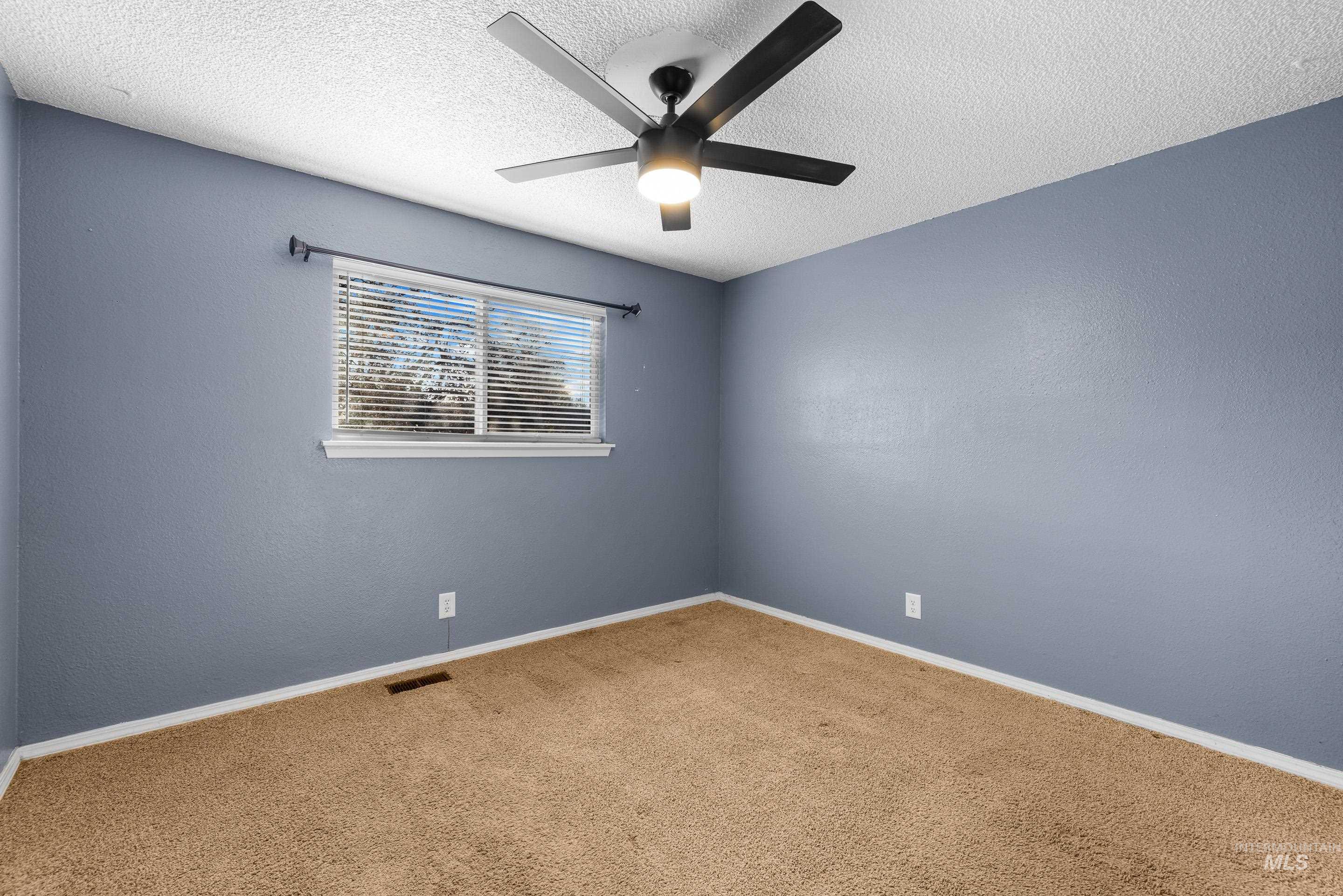 Empty room featuring carpet floors, a textured ceiling, ceiling fan, and a textured wall