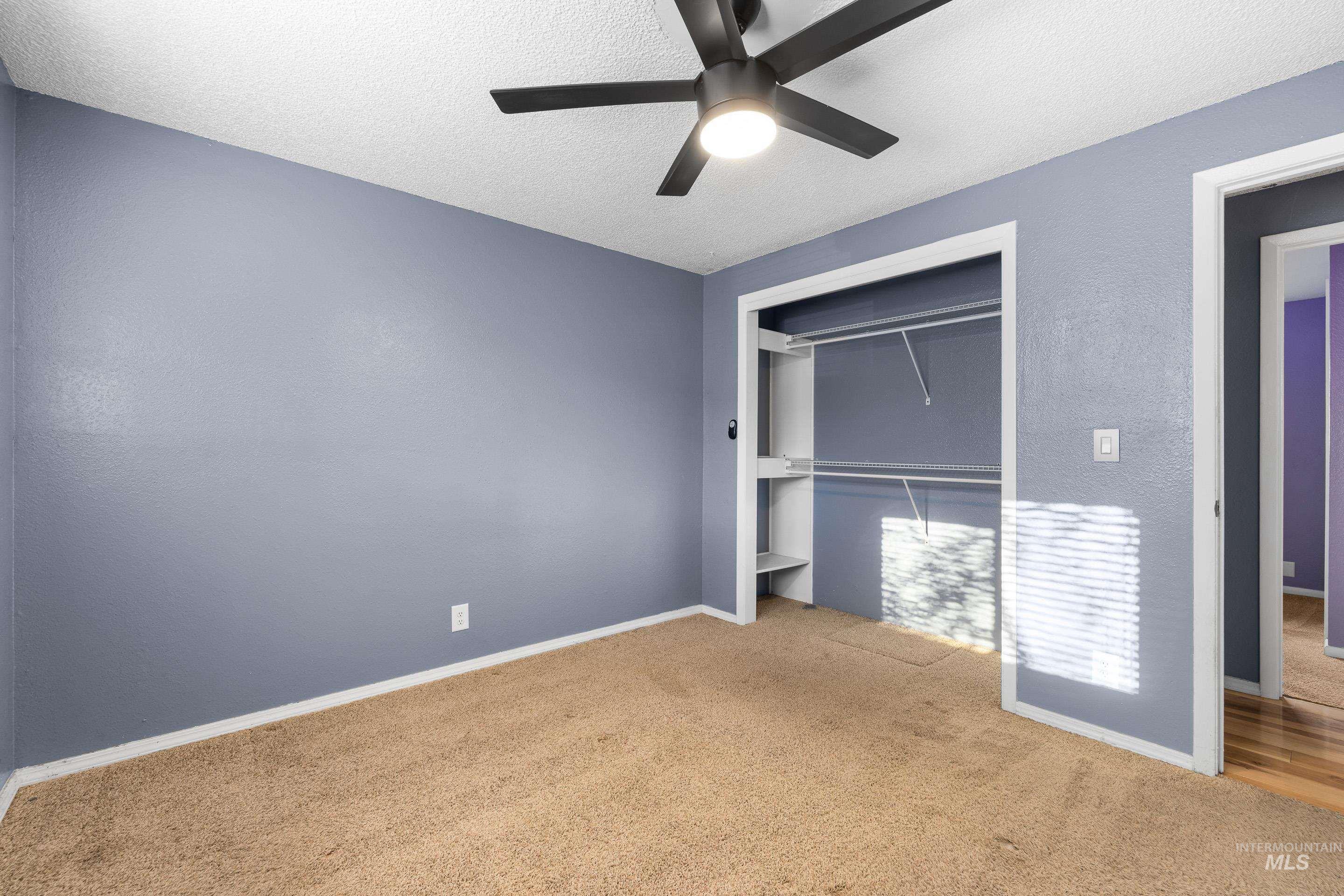 Unfurnished bedroom with carpet floors, a ceiling fan, a textured ceiling, a closet, and a textured wall