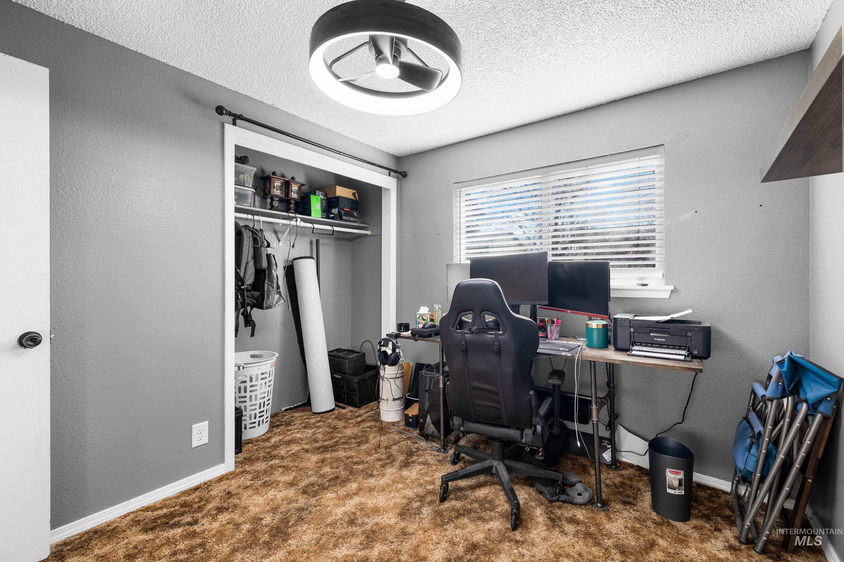 Office area with a textured wall, dark colored carpet, and a textured ceiling