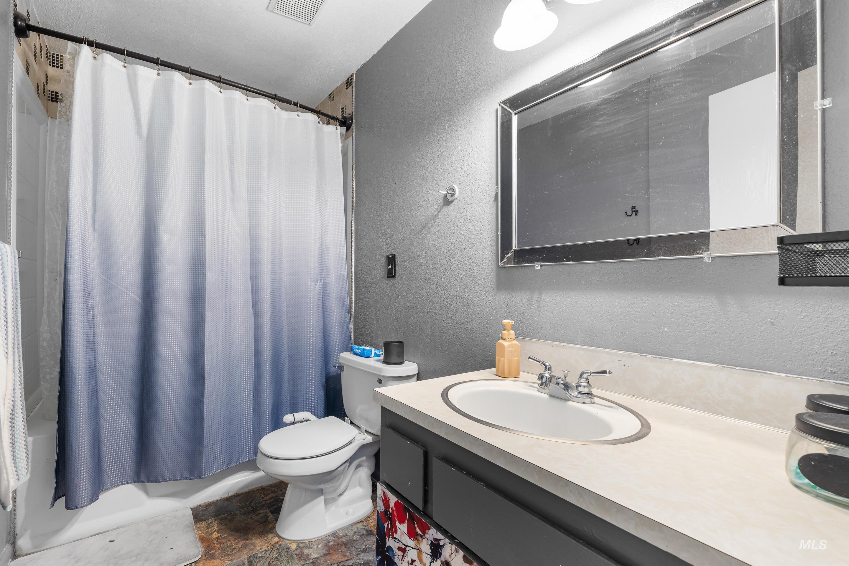 Bathroom featuring a textured wall, vanity, shower / tub combo, and stone tile floors