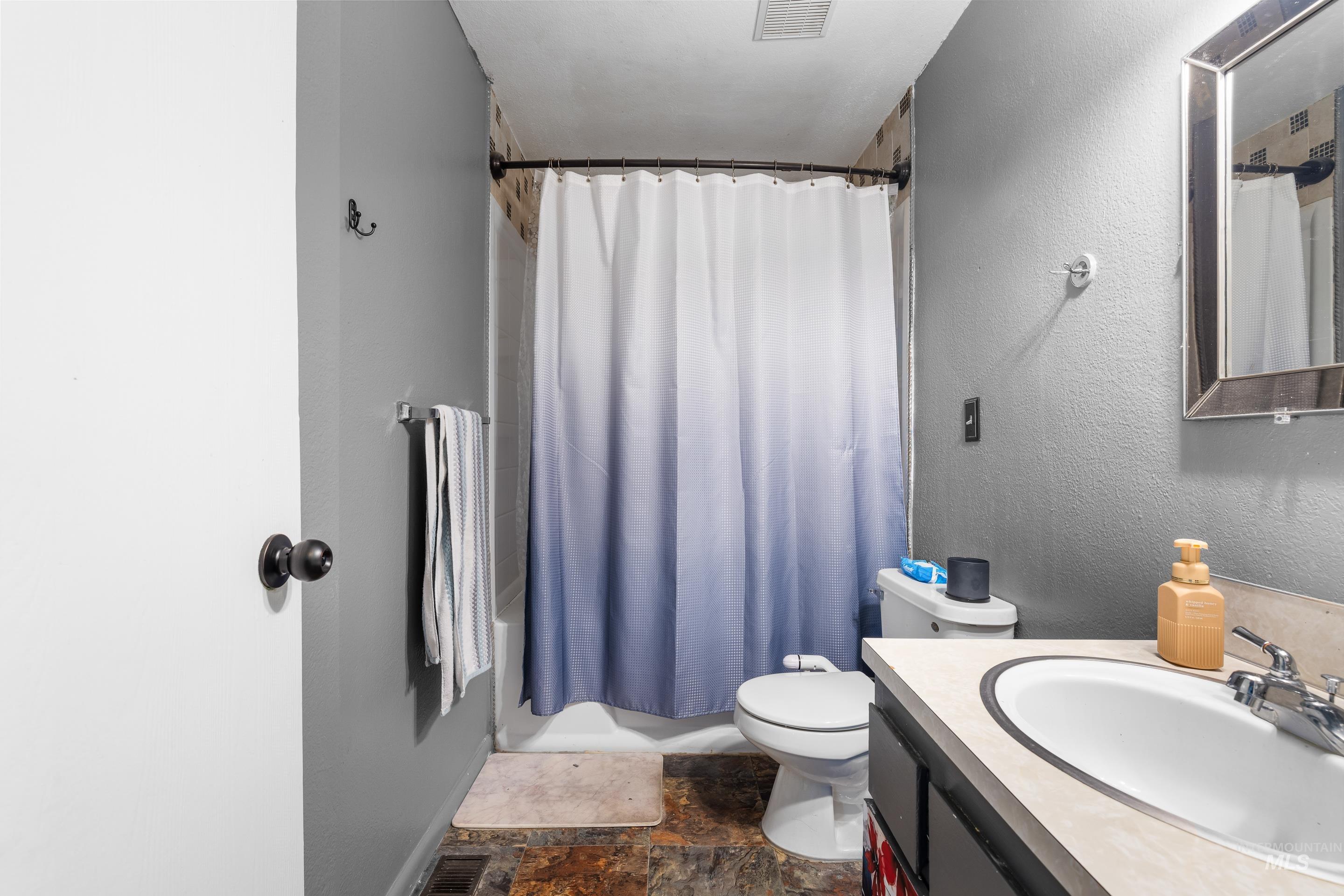 Bathroom with stone tile flooring, vanity, shower / tub combo with curtain, and a textured wall