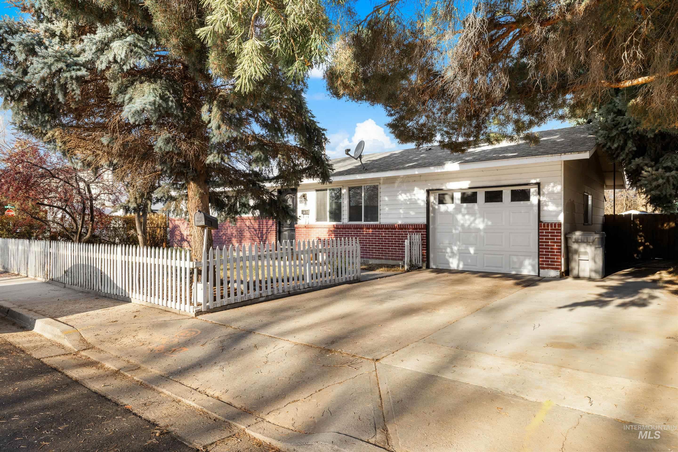 Single story home with brick siding, a fenced front yard, an attached garage, and driveway