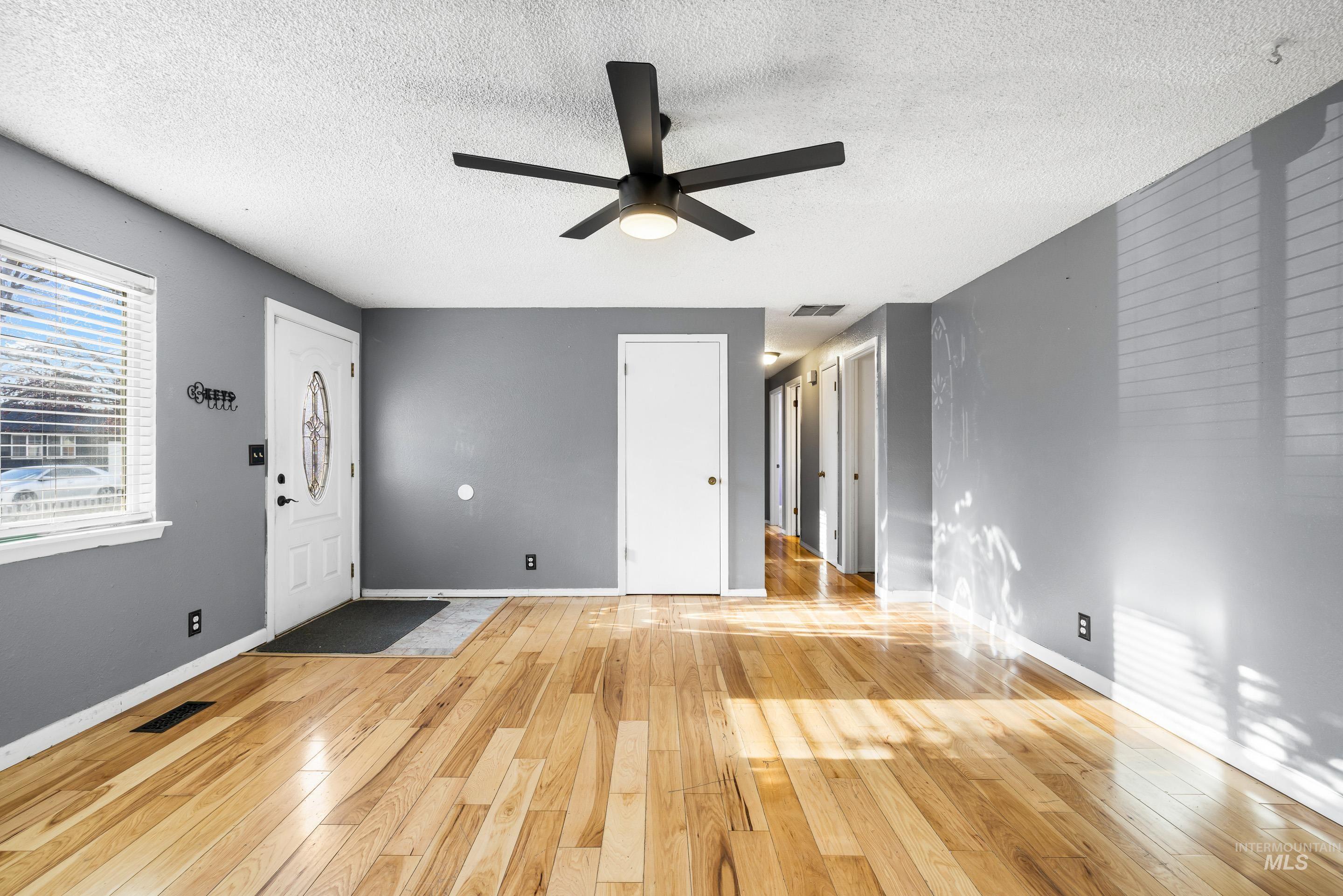 Unfurnished living room with light wood-style flooring, a textured ceiling, and ceiling fan