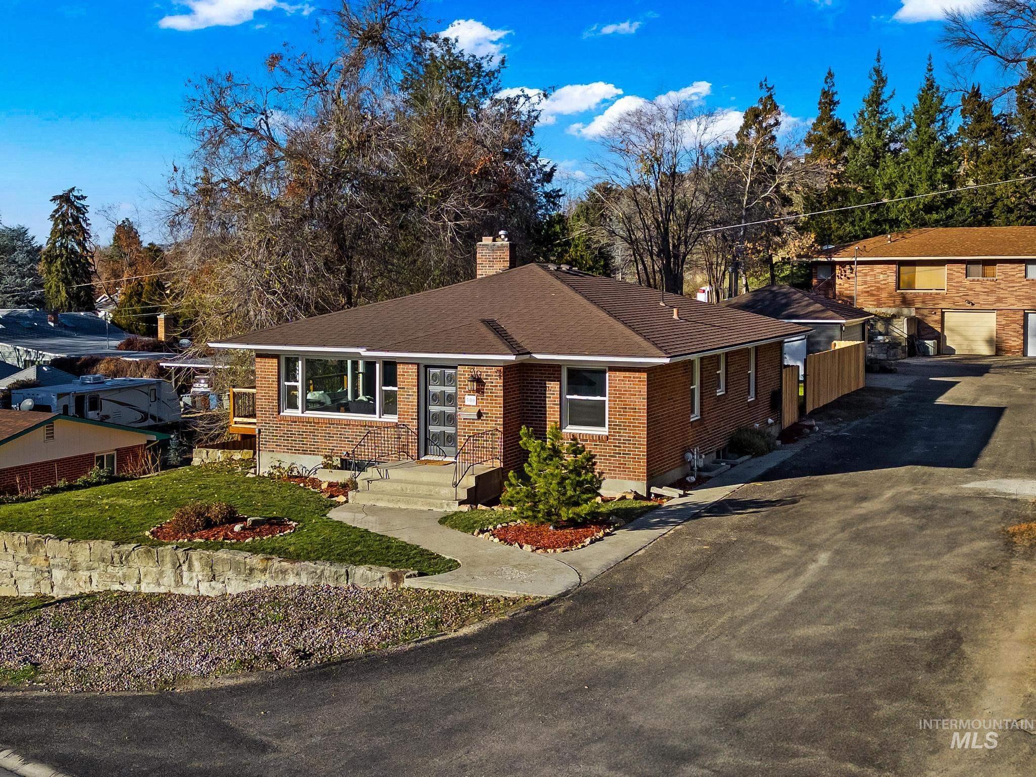 View of front of property featuring a chimney, brick siding, a shingled roof, asphalt driveway, and a front lawn