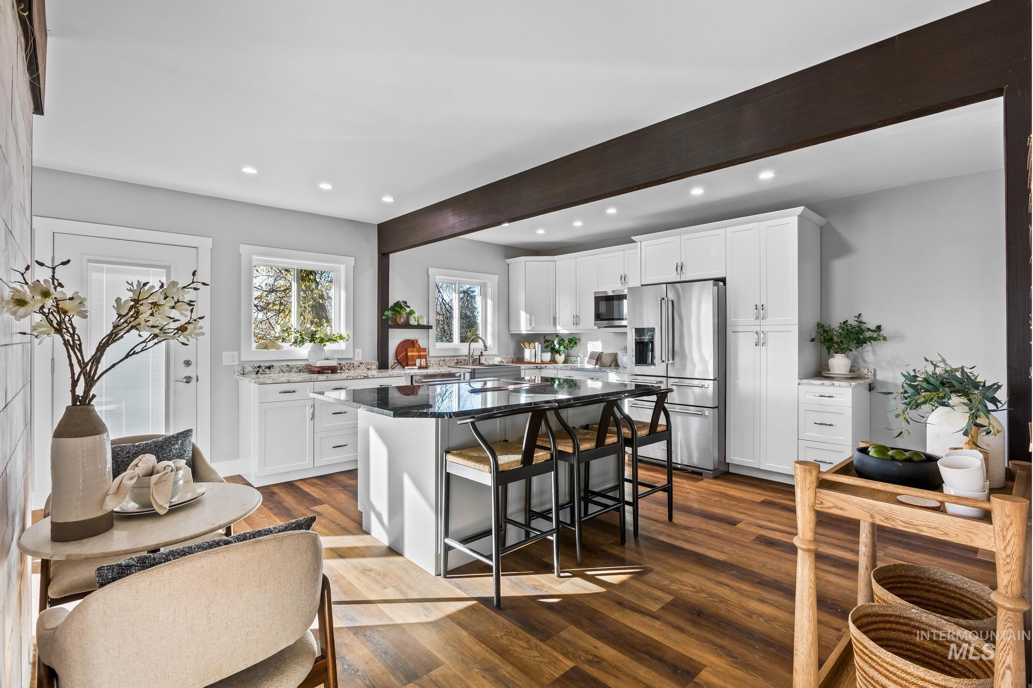 Kitchen with beamed ceiling, white cabinets, appliances with stainless steel finishes, dark stone countertops, and a breakfast bar area