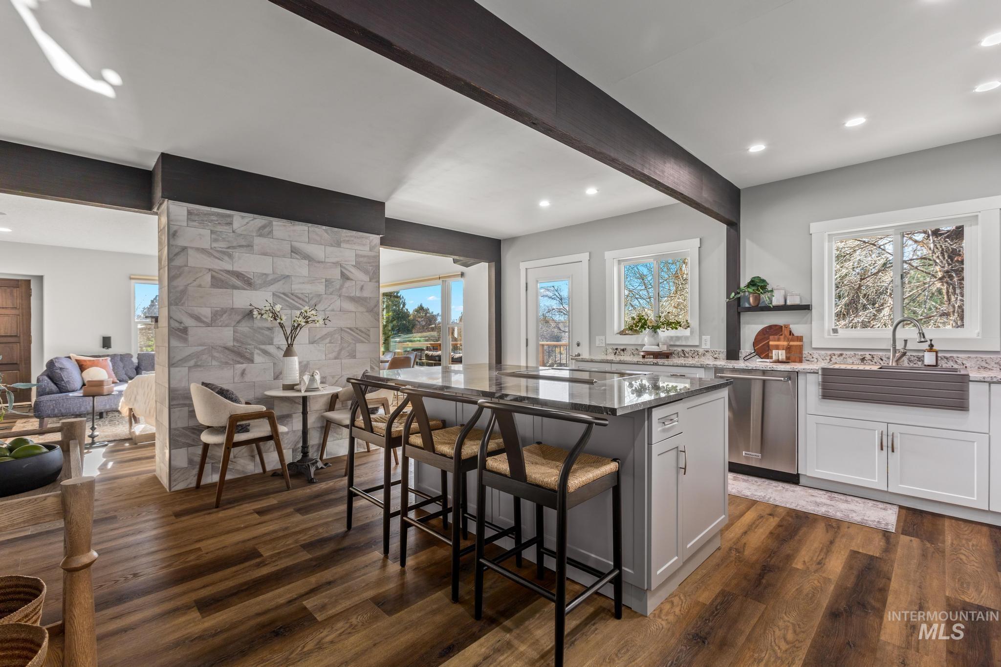 Kitchen featuring light stone countertops, a kitchen island, beam ceiling, stainless steel dishwasher, and a breakfast bar area