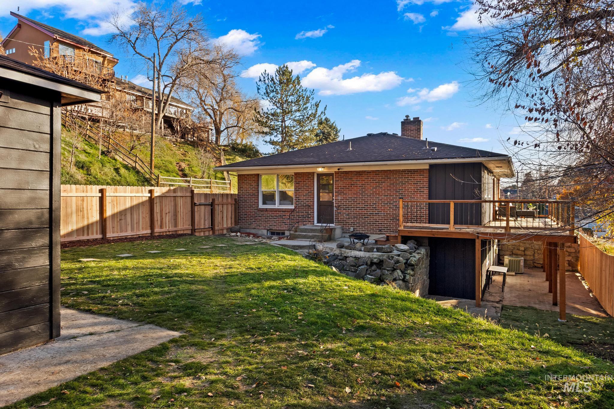 Back of house featuring a patio, a chimney, a fenced backyard, brick siding, and a wooden deck