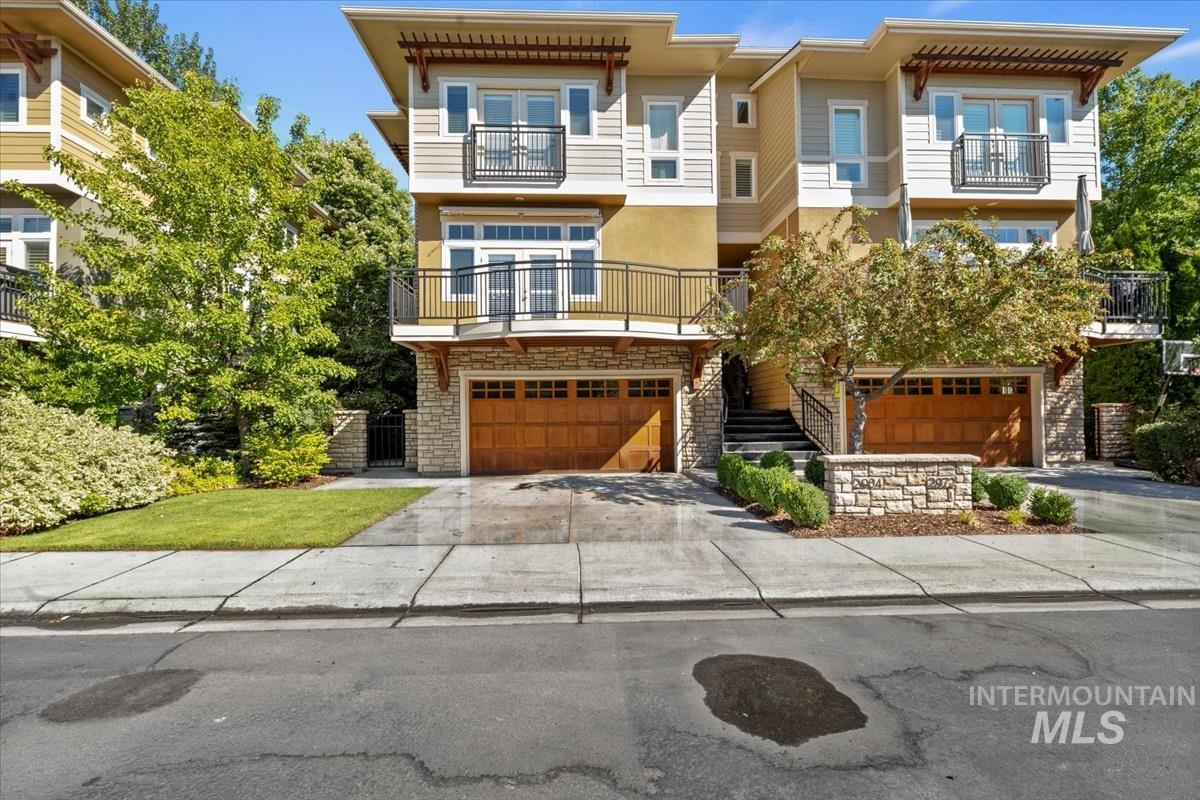 View of front of house with stone siding, a balcony, an attached garage, driveway, and stucco siding