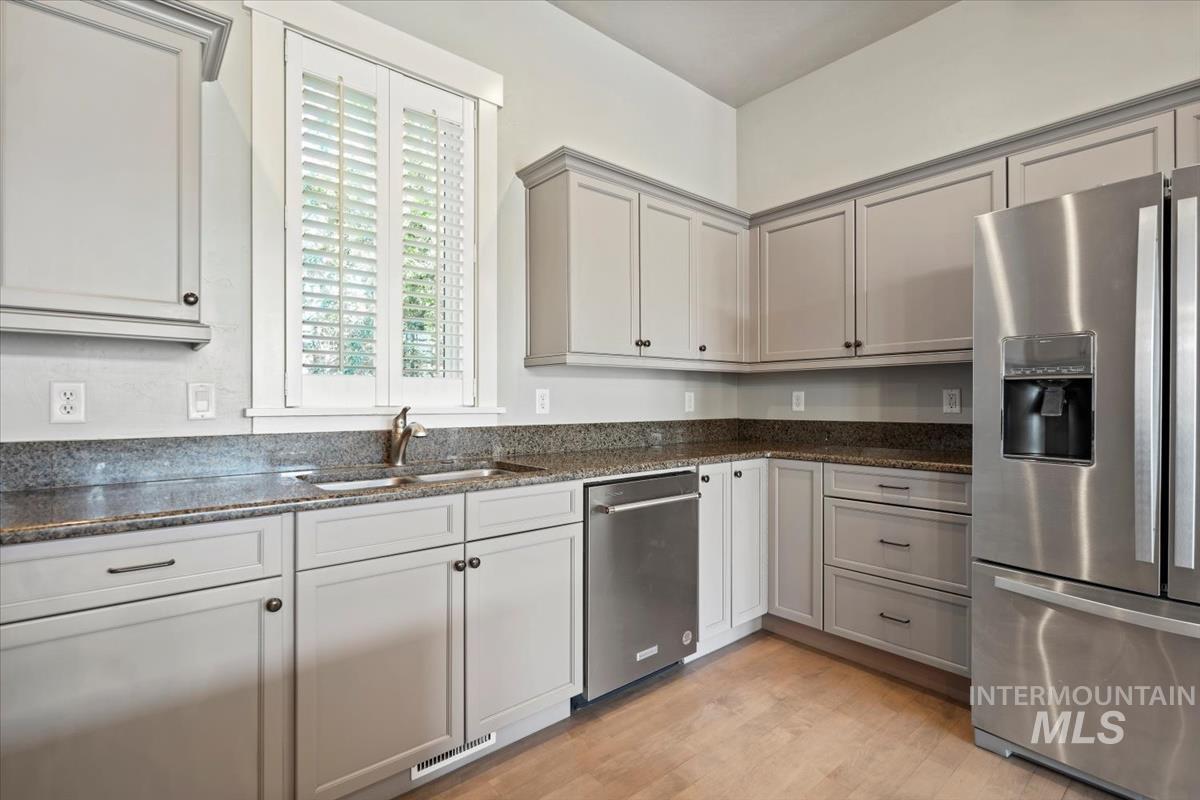 Kitchen with appliances with stainless steel finishes, dark stone countertops, light wood-type flooring, and gray cabinets