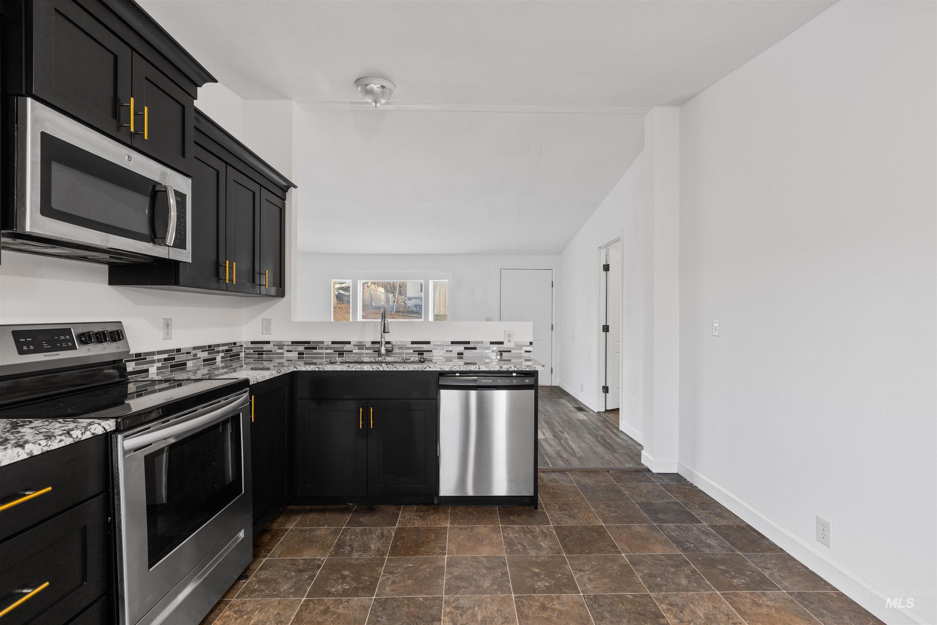 Kitchen featuring dark cabinets, stainless steel appliances, stone finish floors, a peninsula, and light stone countertops