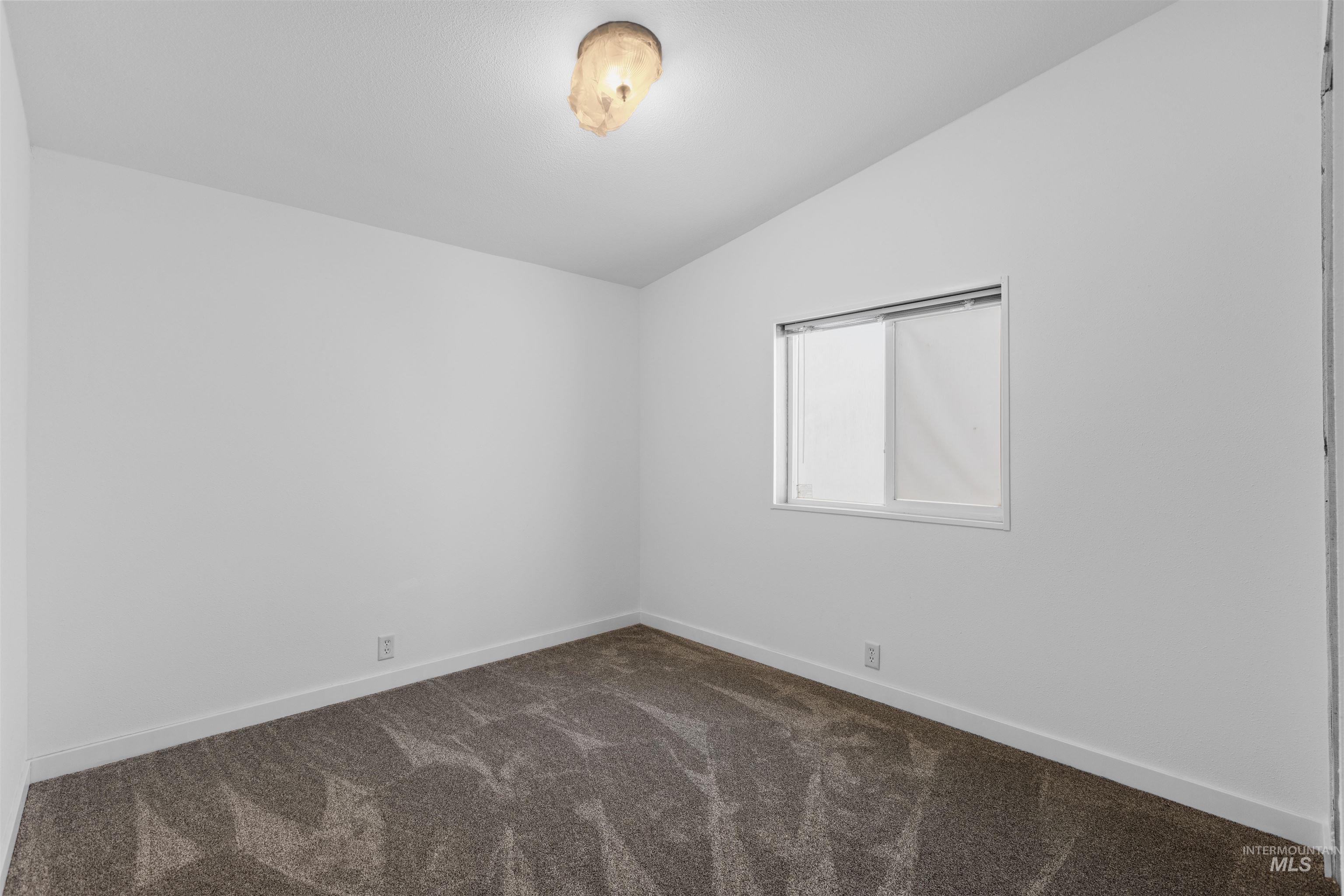 Spare room featuring vaulted ceiling and dark colored carpet