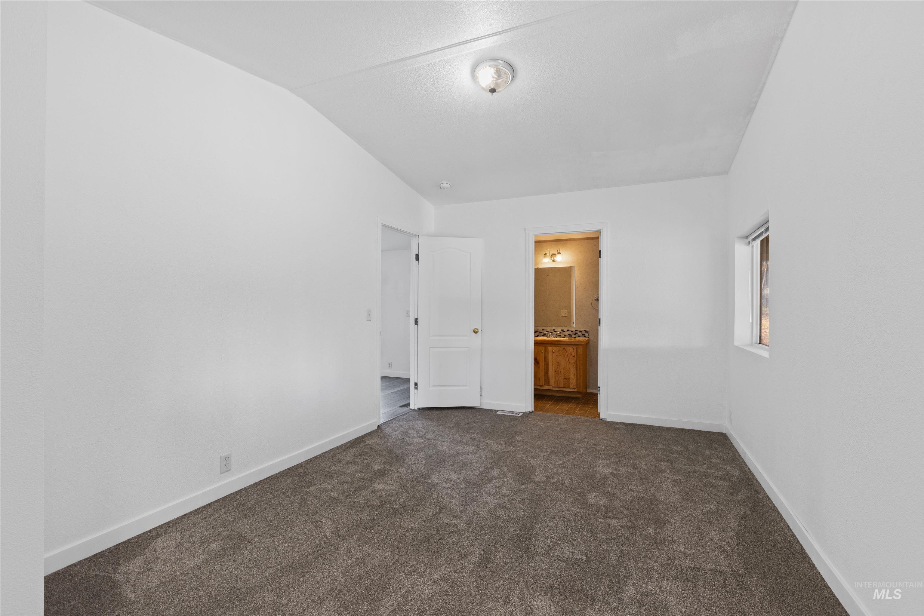 Unfurnished bedroom featuring dark colored carpet, ensuite bath, and lofted ceiling