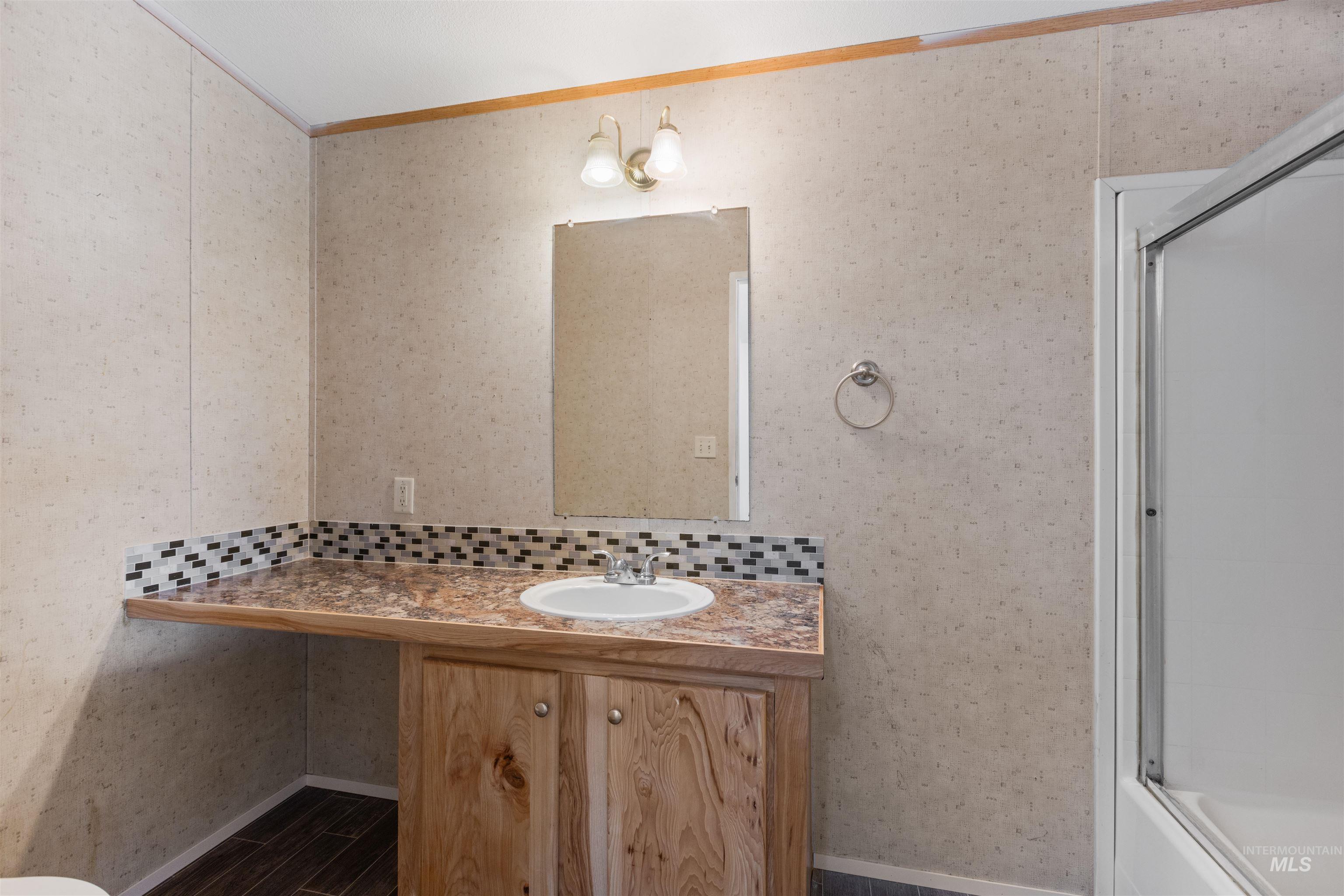 Full bath featuring wallpapered walls, vanity, crown molding, dark wood-style floors, and bath / shower combo with glass door