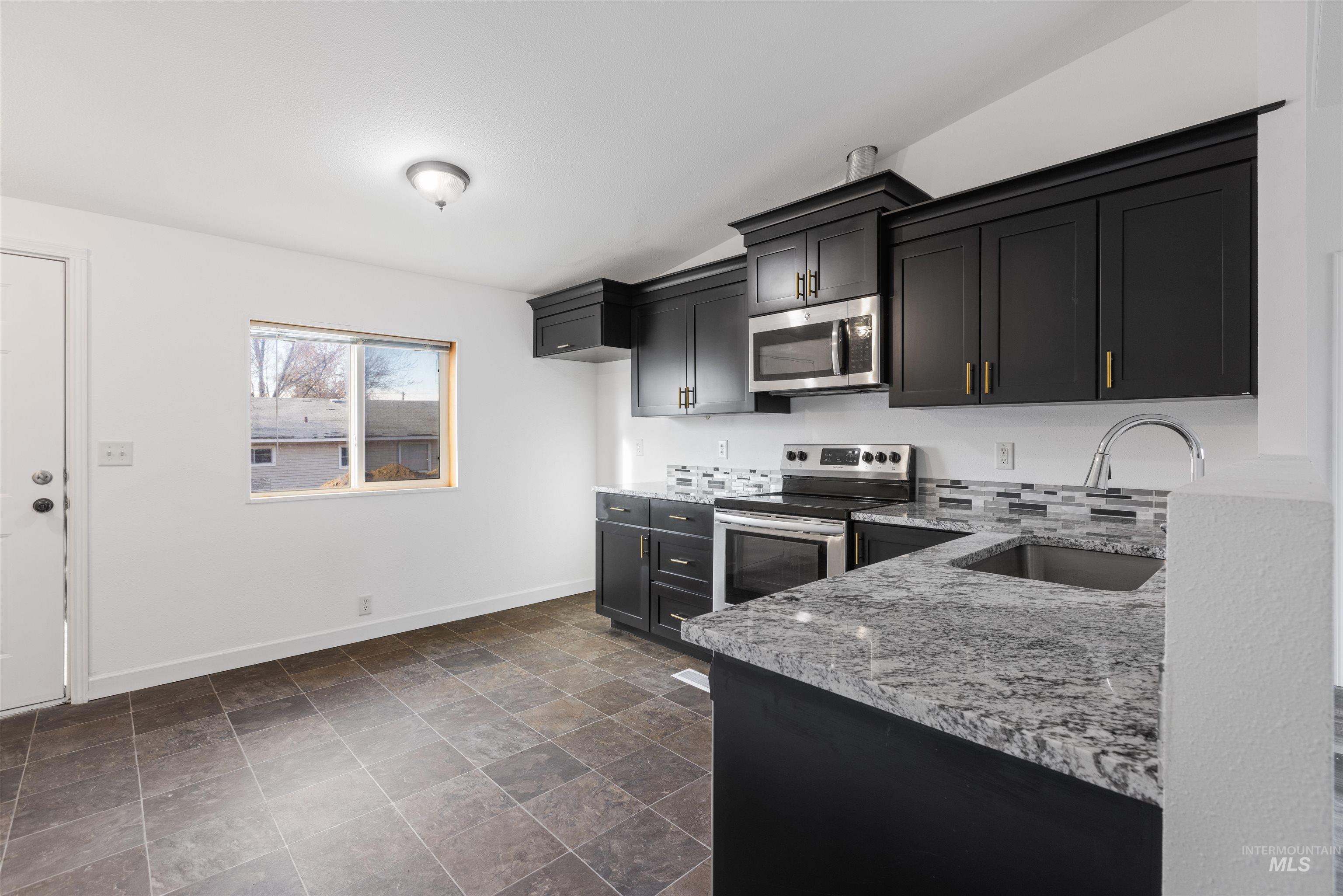 Kitchen featuring light stone counters, appliances with stainless steel finishes, dark cabinets, and stone finish floors