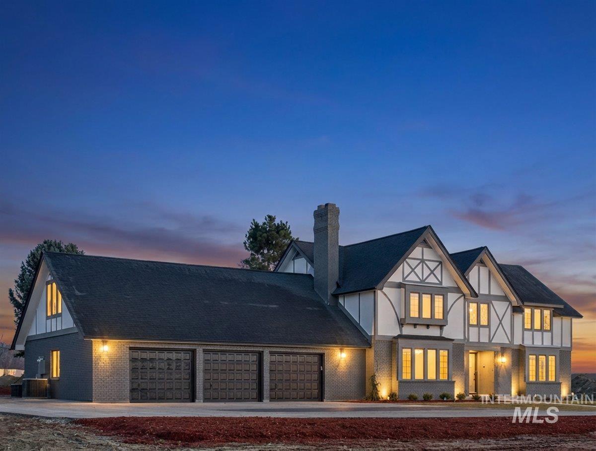 Tudor home with brick siding, a chimney, board and batten siding, an attached garage, and driveway
