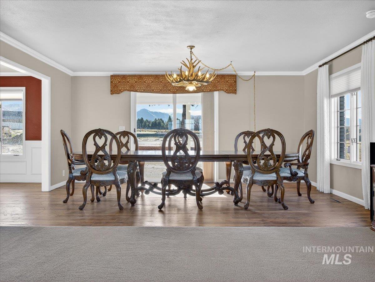 Dining room with wood finished floors, plenty of natural light, ornamental molding, a chandelier, and a wainscoted wall
