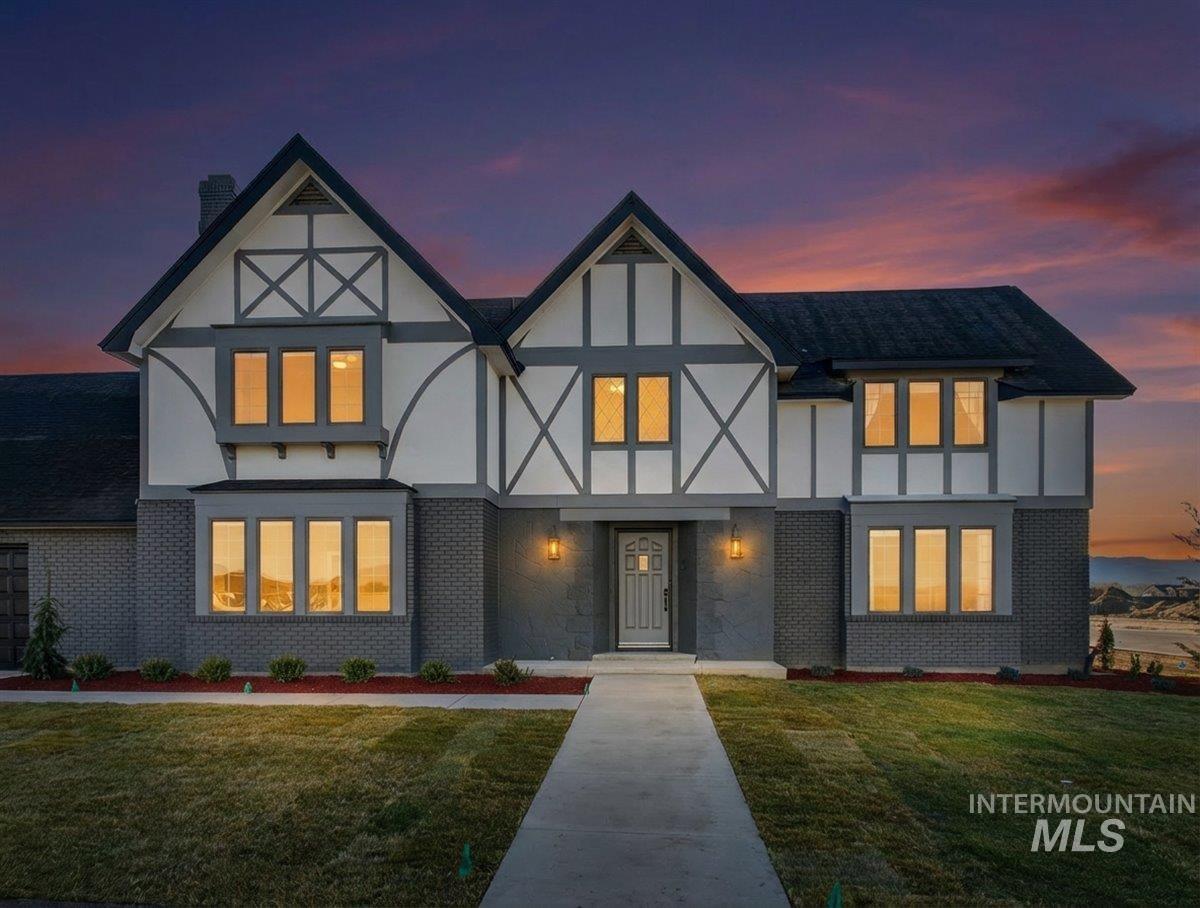 Tudor-style house featuring a chimney, brick siding, a front lawn, and stucco siding