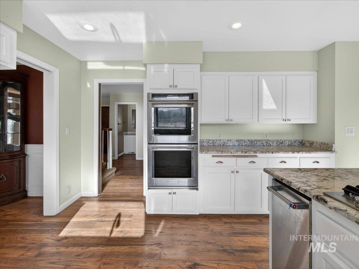 Kitchen with light stone counters, appliances with stainless steel finishes, white cabinets, dark wood finished floors, and recessed lighting