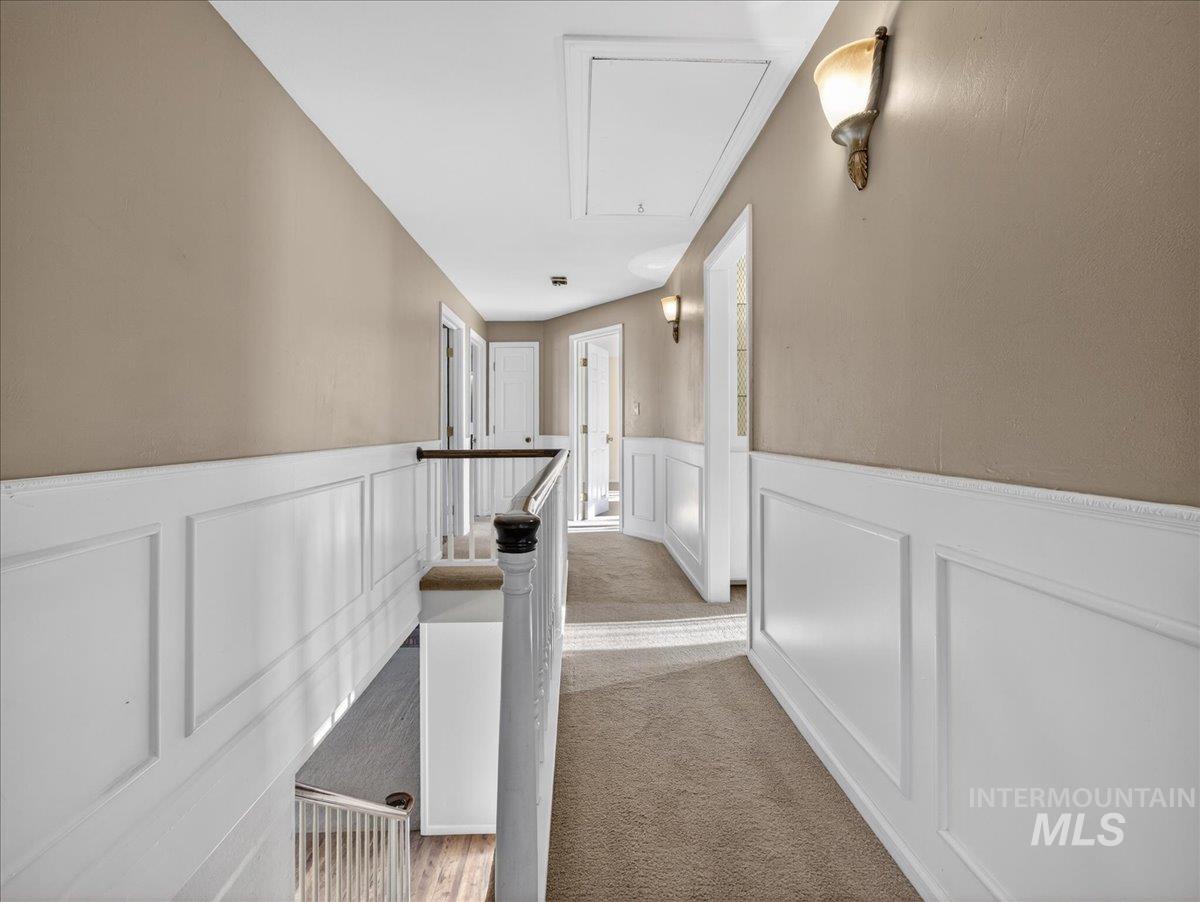 Hall featuring attic access, an upstairs landing, a wainscoted wall, a decorative wall, and light colored carpet