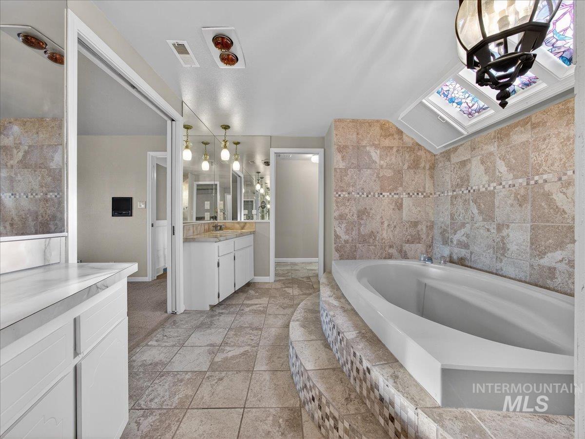Bathroom with a chandelier, a bath, vanity, and lofted ceiling