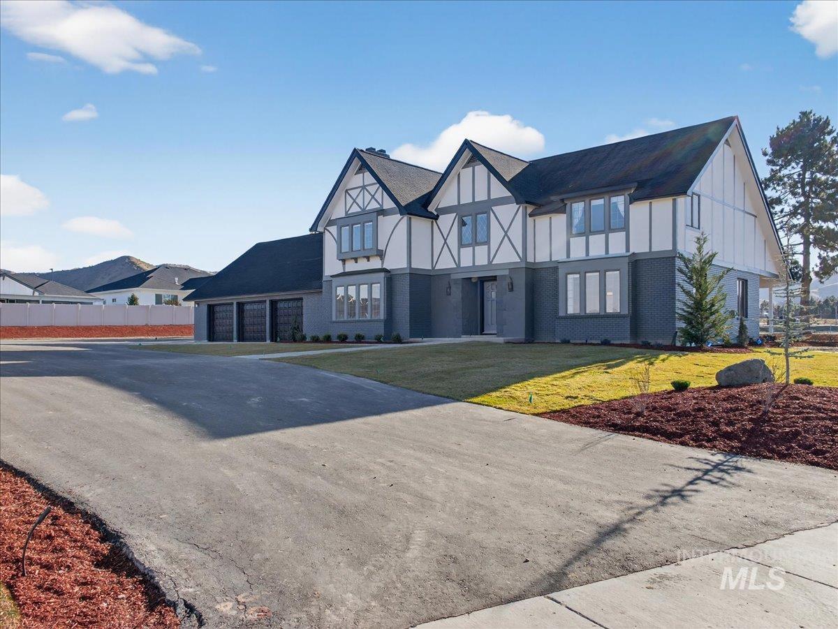 Tudor house featuring asphalt driveway, a front lawn, brick siding, and board and batten siding