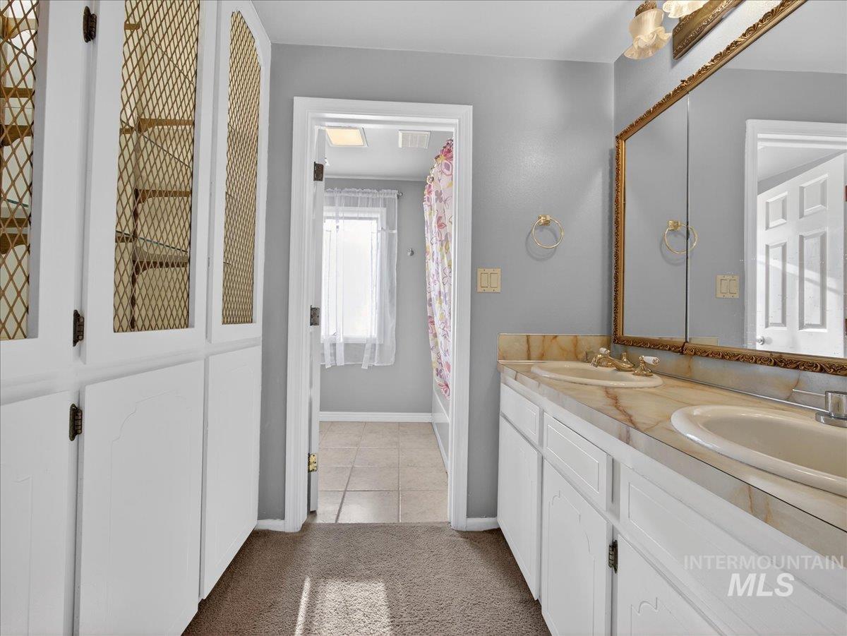 Bathroom featuring double vanity, shower / bath combo with shower curtain, light carpet, and light tile patterned floors