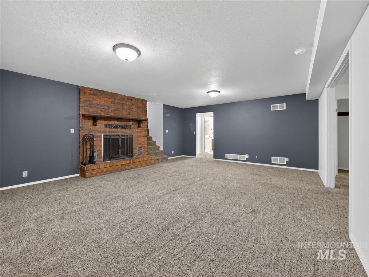 Unfurnished living room featuring a brick fireplace, a textured ceiling, and carpet