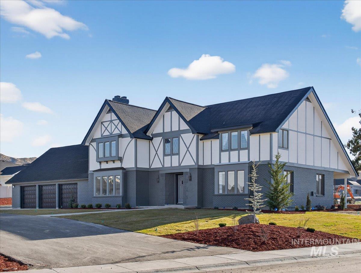 Tudor-style house with brick siding, a front yard, driveway, and a chimney