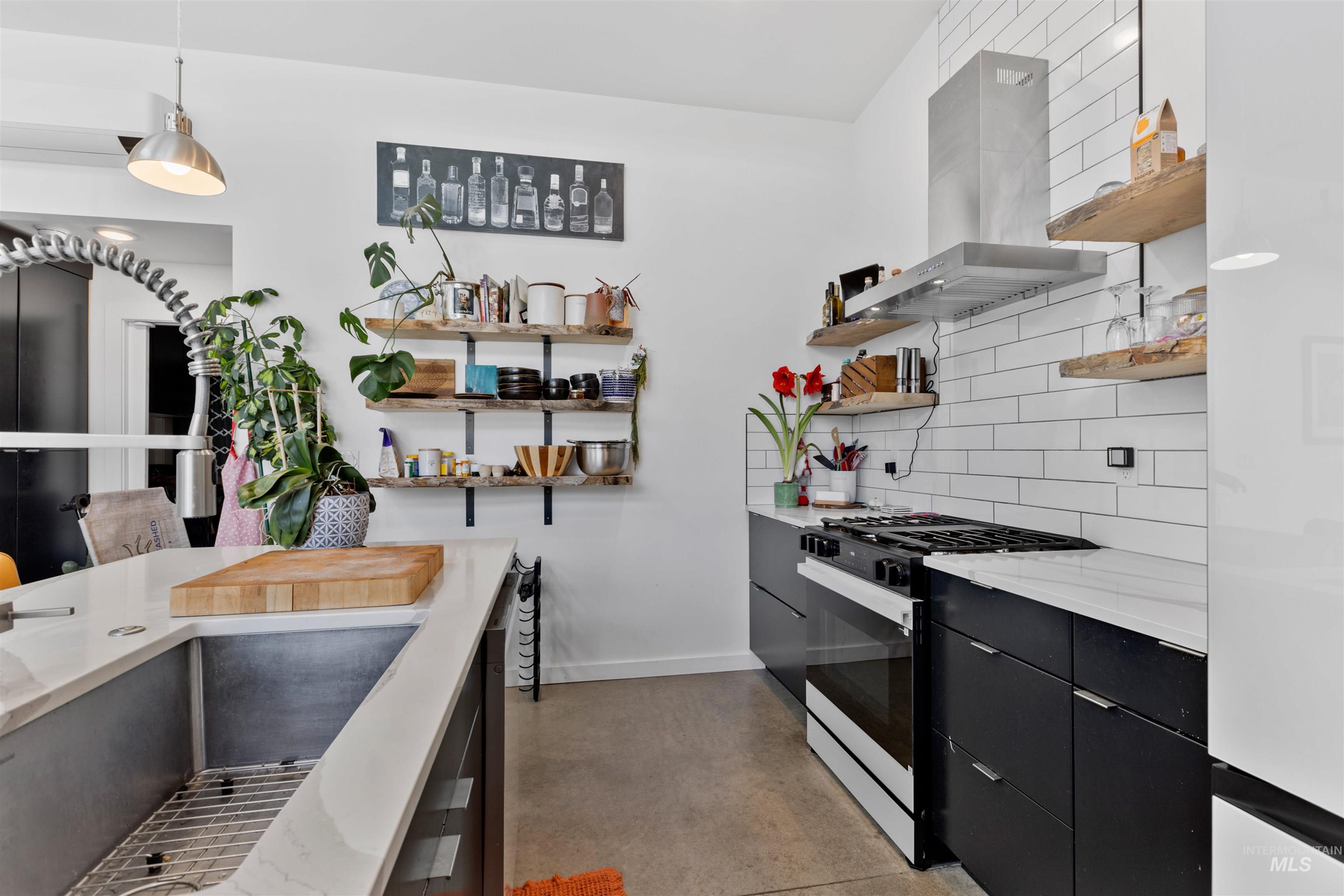 Kitchen featuring dark cabinetry, range with gas cooktop, tasteful backsplash, hanging light fixtures, and island exhaust hood