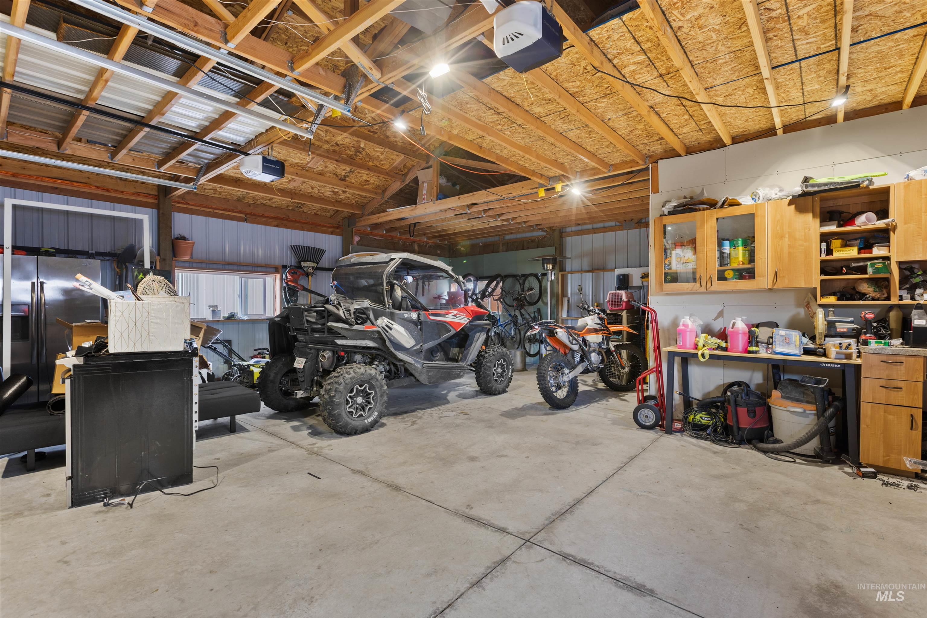 Garage with stainless steel refrigerator with ice dispenser, a garage door opener, and metal wall