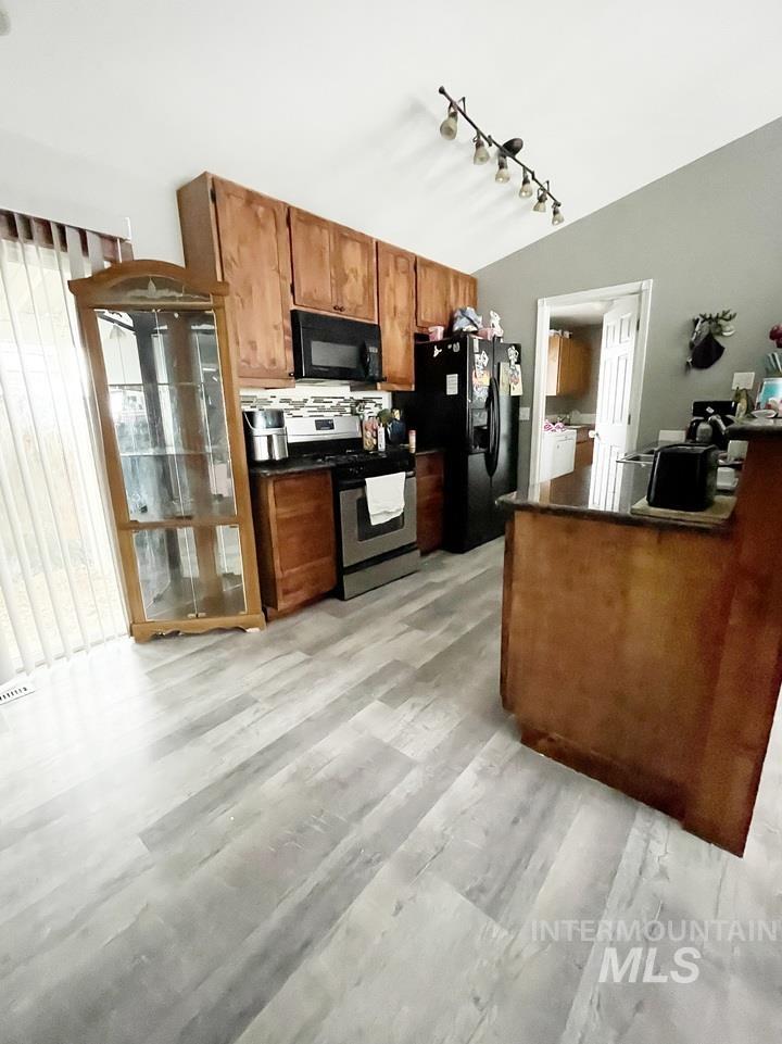 Kitchen with brown cabinetry, black appliances, a peninsula, light wood finished floors, and rail lighting