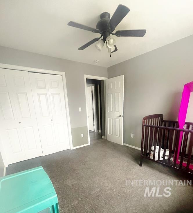 Carpeted bedroom featuring a crib, ceiling fan, and a closet
