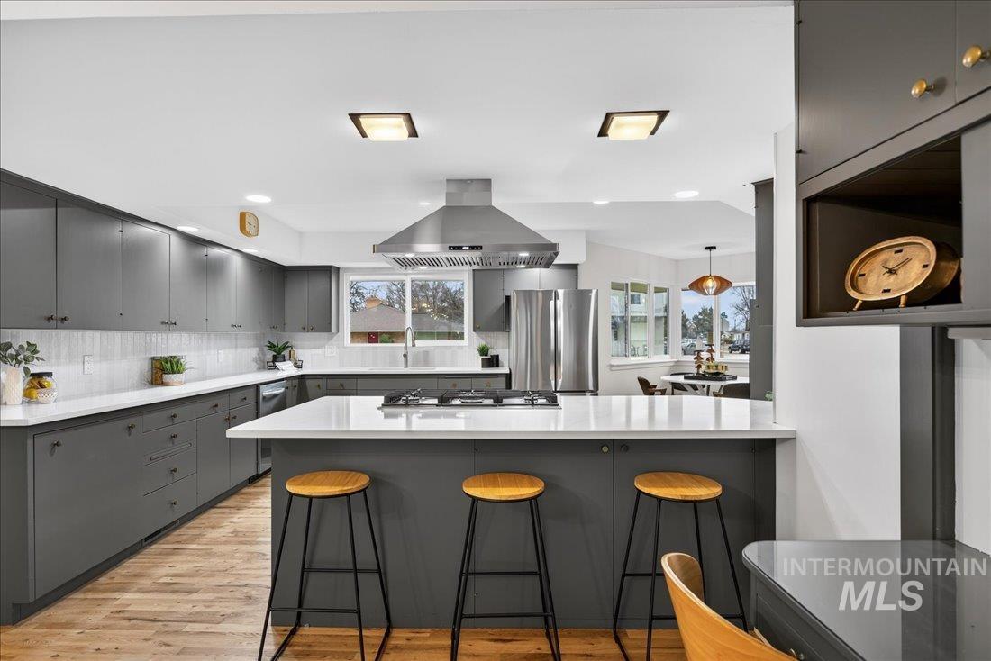Kitchen featuring a kitchen bar, gray cabinetry, island range hood, stainless steel appliances, and light wood-style flooring
