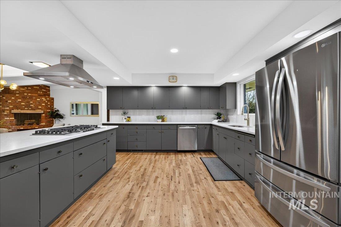 Kitchen with stainless steel appliances, island exhaust hood, light countertops, gray cabinetry, and recessed lighting