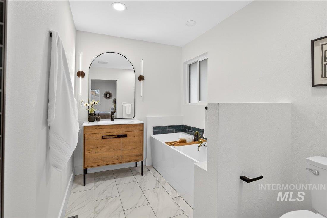 Bathroom with a garden tub, light marble finish floors, and vanity