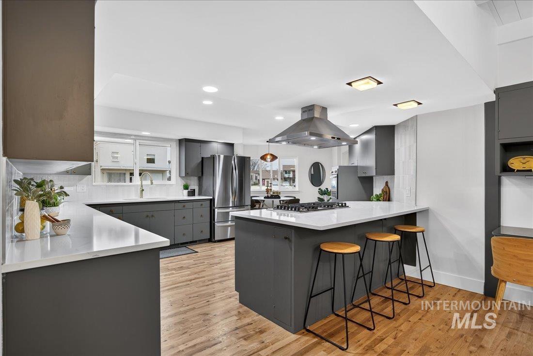Kitchen with gray cabinets, a breakfast bar, freestanding refrigerator, island exhaust hood, and light wood finished floors