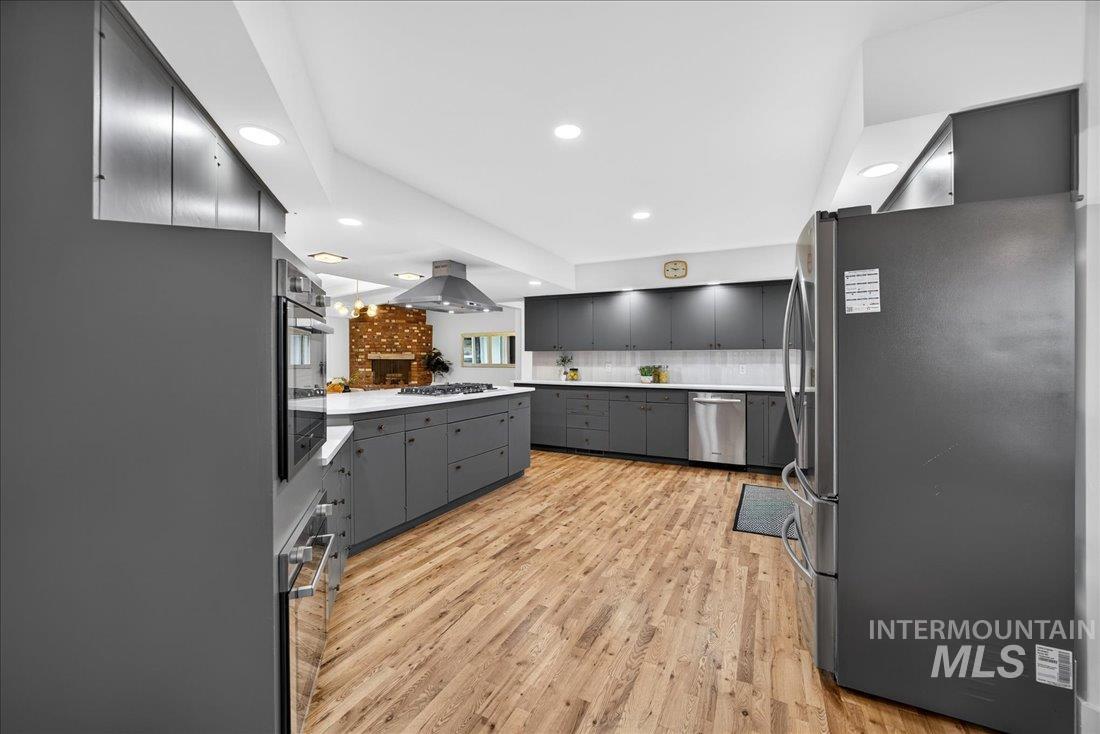 Kitchen with gray cabinets, appliances with stainless steel finishes, light wood-style floors, island exhaust hood, and light countertops