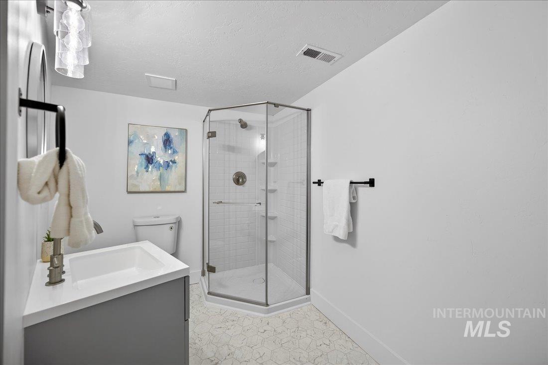 Full bathroom with vanity, a shower stall, a textured ceiling, and light flooring