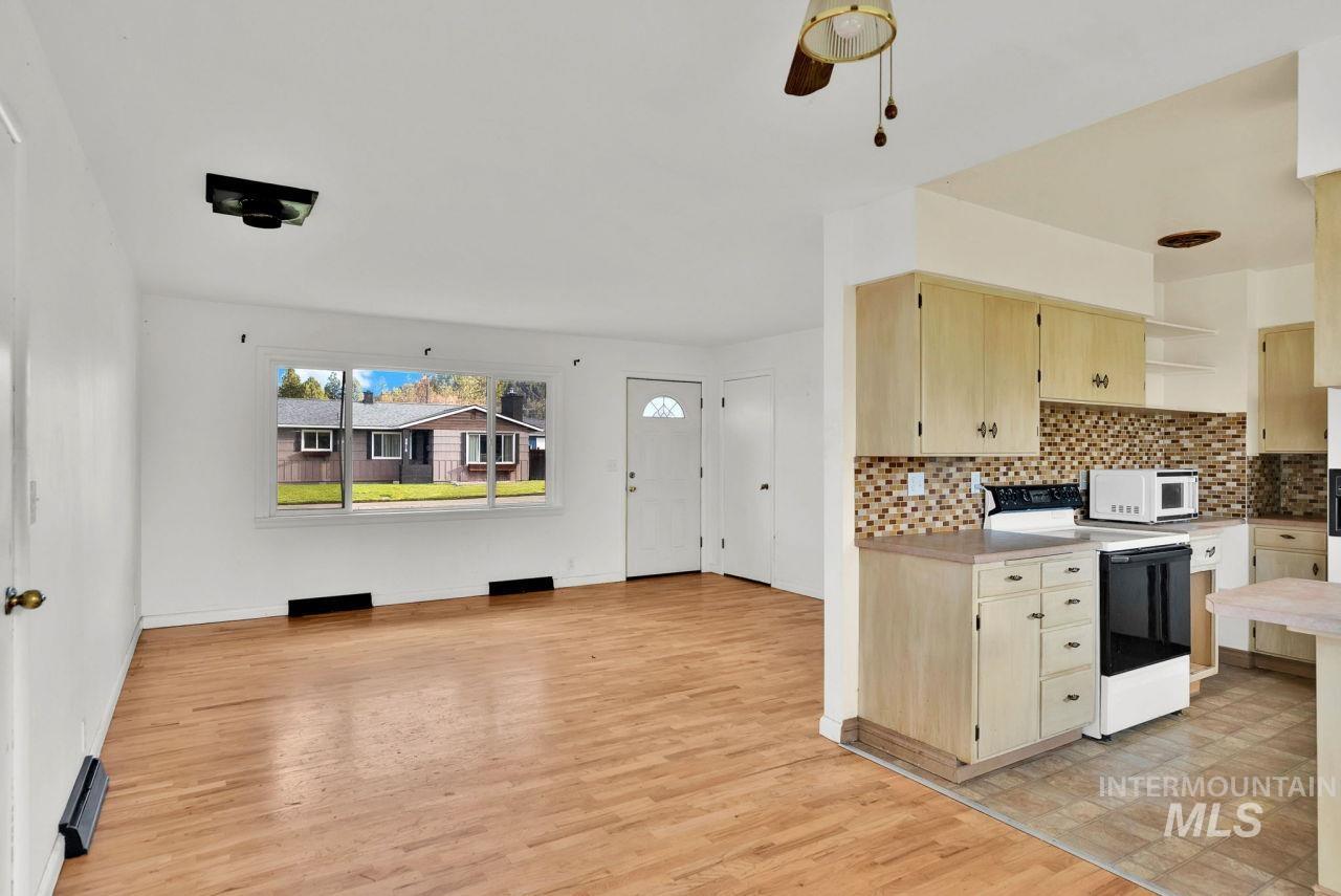 Kitchen with electric range, light countertops, open shelves, backsplash, and light wood finished floors