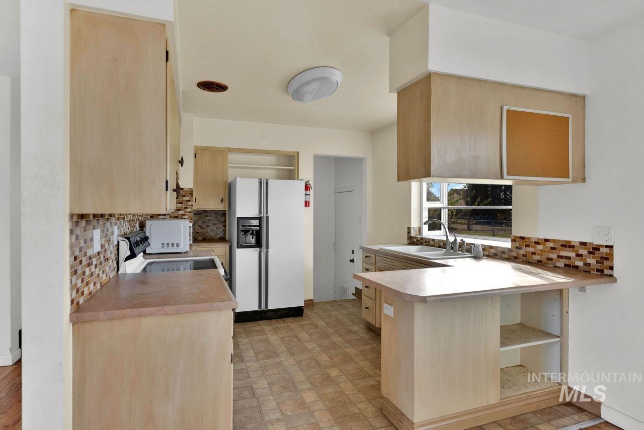 Kitchen with a peninsula, white appliances, light brown cabinetry, light countertops, and backsplash